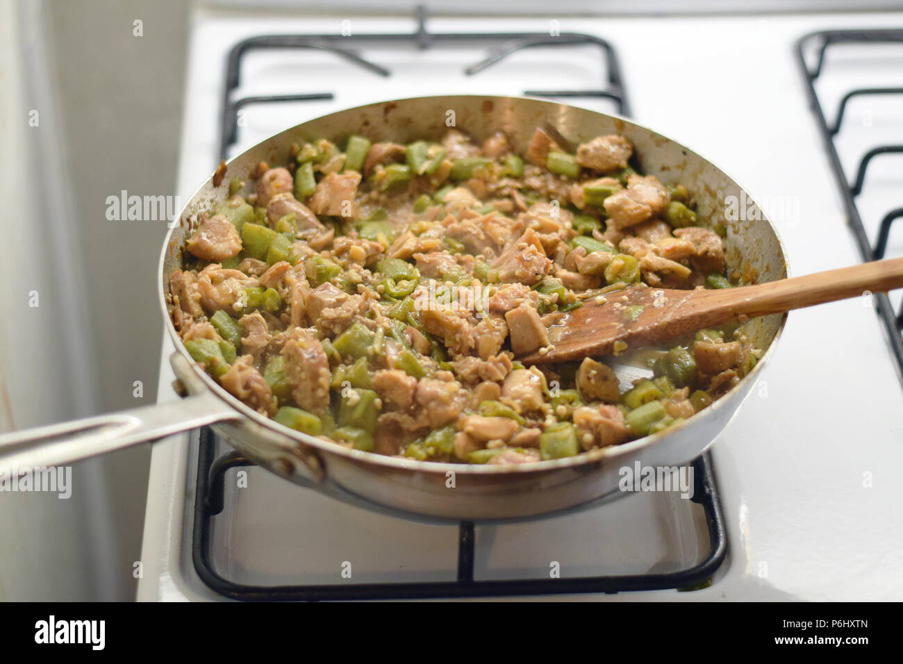 Spatola in legno agitazione frango com quiabo (Portoghese per 'pollo con okra'), Brasiliano piatto di cottura far saltare in padella sulla stufa Foto Stock