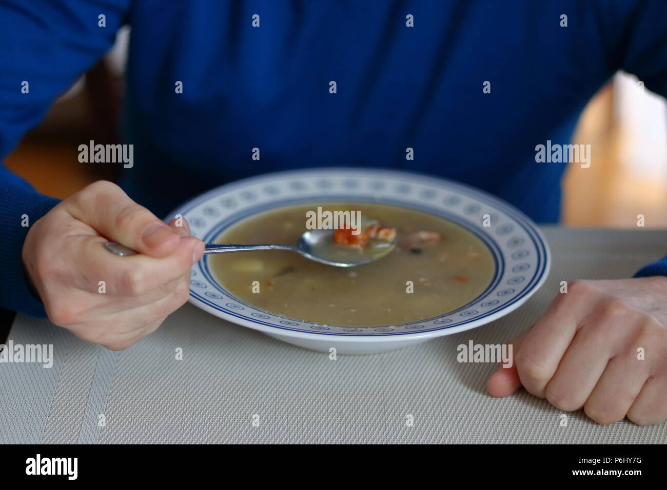 Uomo si siede a tavola da soli e si mangia la minestra, piastra con minestra sulla tavola, uomo vestito in blu maglione Foto Stock