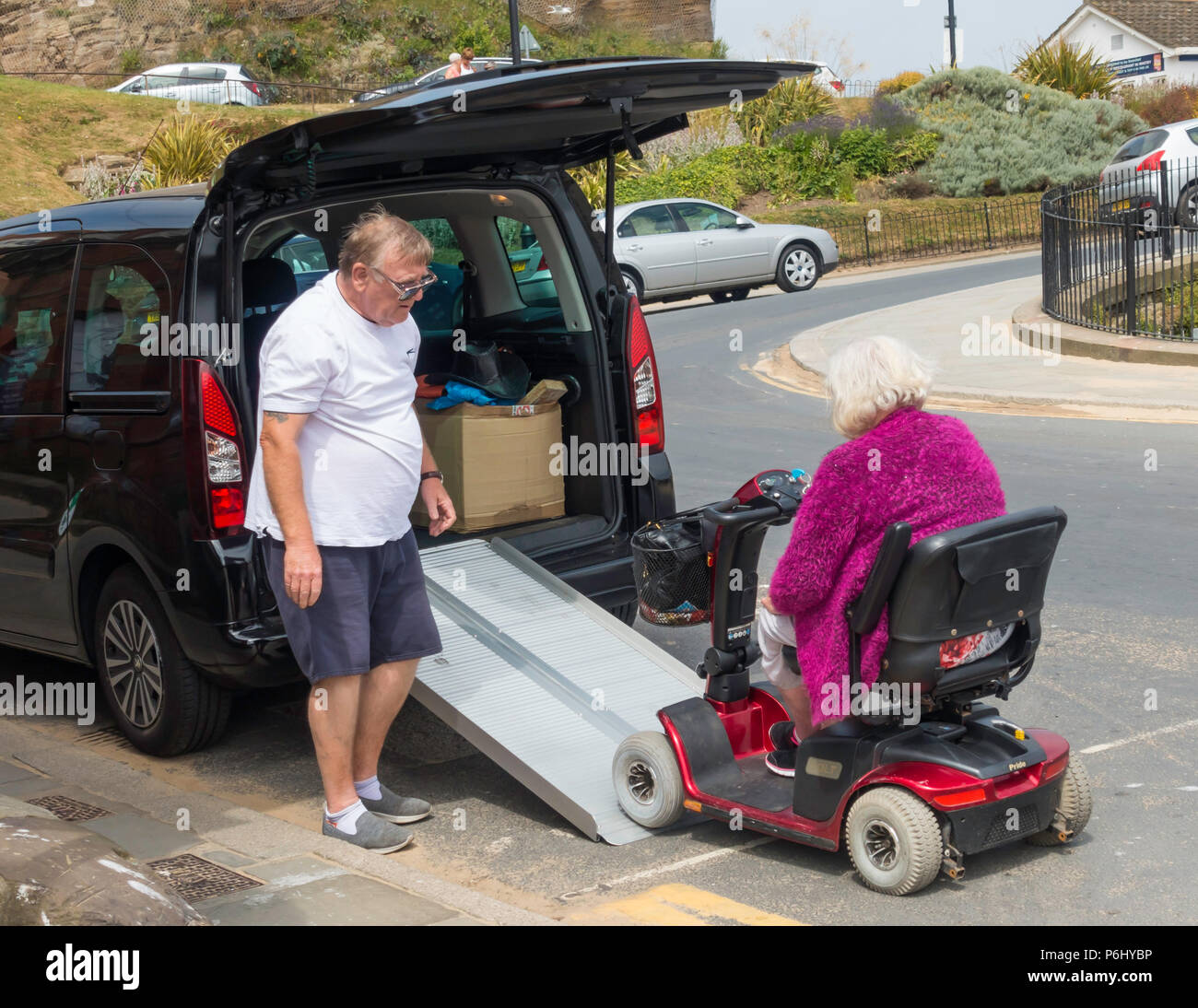 Una signora anziana la sua unità mobility scooter fino a rampa portatile in un taxi sotto l'occhio vigile del taxi driver Foto Stock