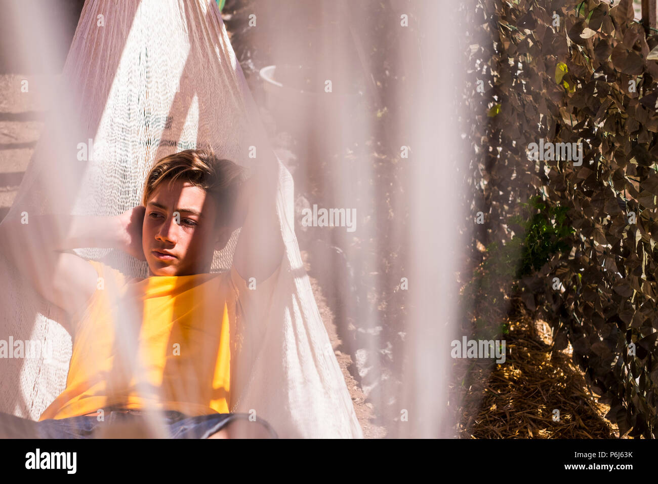 Bella caucasian giovane ragazzo in soggiorno e poggiare su un amaca all'aperto in natura. espressione seria faccia per periodo di adolescente e l'età. Foto Stock