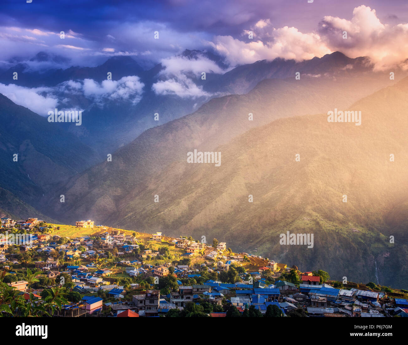 Piccolo villaggio sulla collina illuminata da un sole al tramonto in Nepal. Paesaggio colorato con case, viola il cielo di nuvole, oro e luce solare ad alta moun Foto Stock