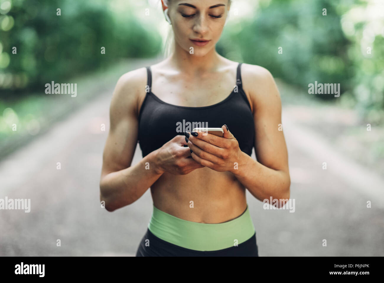 Runner donna nella mattinata estiva Park ascoltare musica sullo smartphone  utilizzando gli auricolari Bluetooth. Femmina ragazza Fitness jogging sul  percorso esterno Foto stock - Alamy