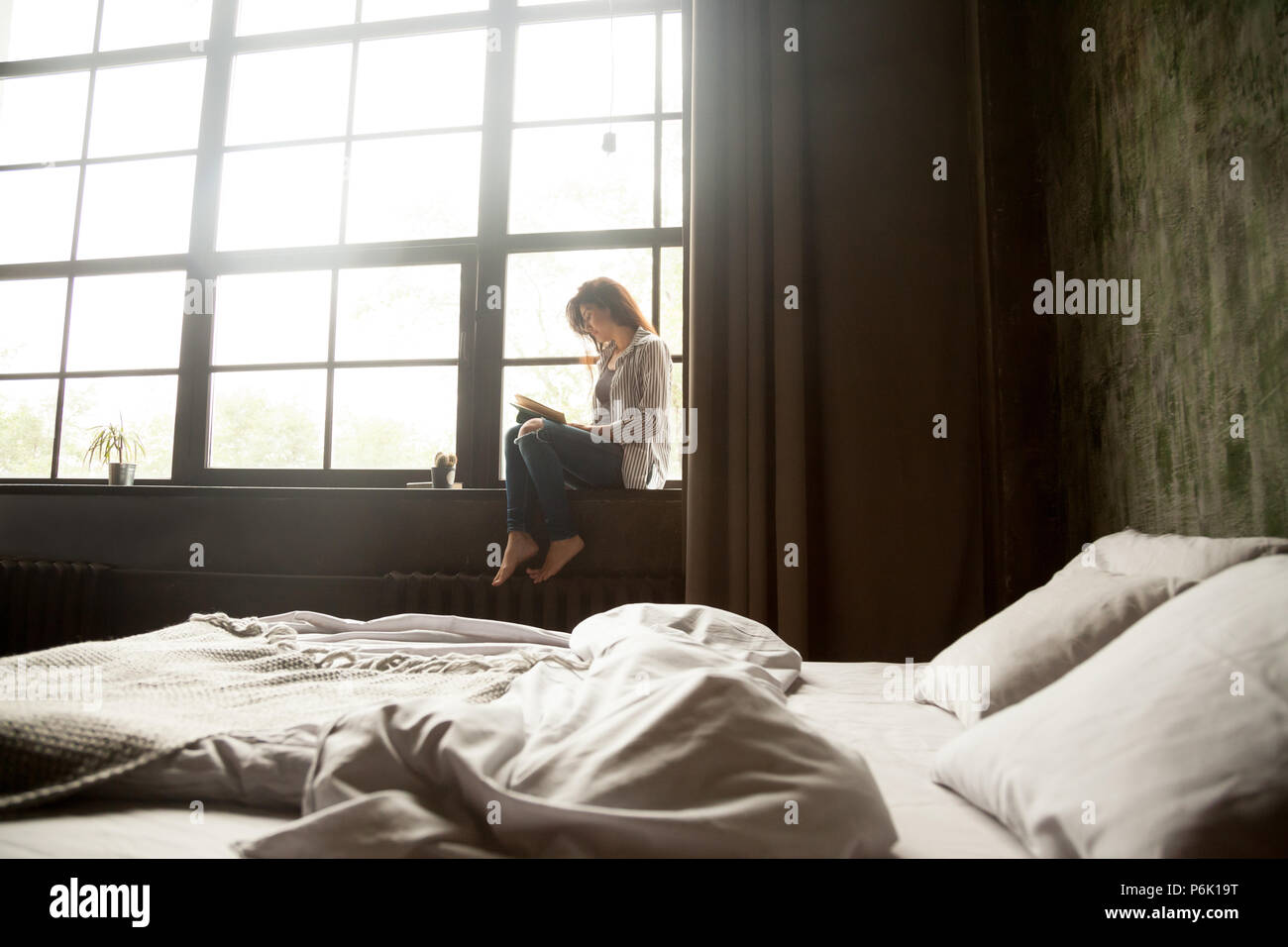 Ragazza giovane lettura libro seduti sul davanzale in camera da letto Foto Stock