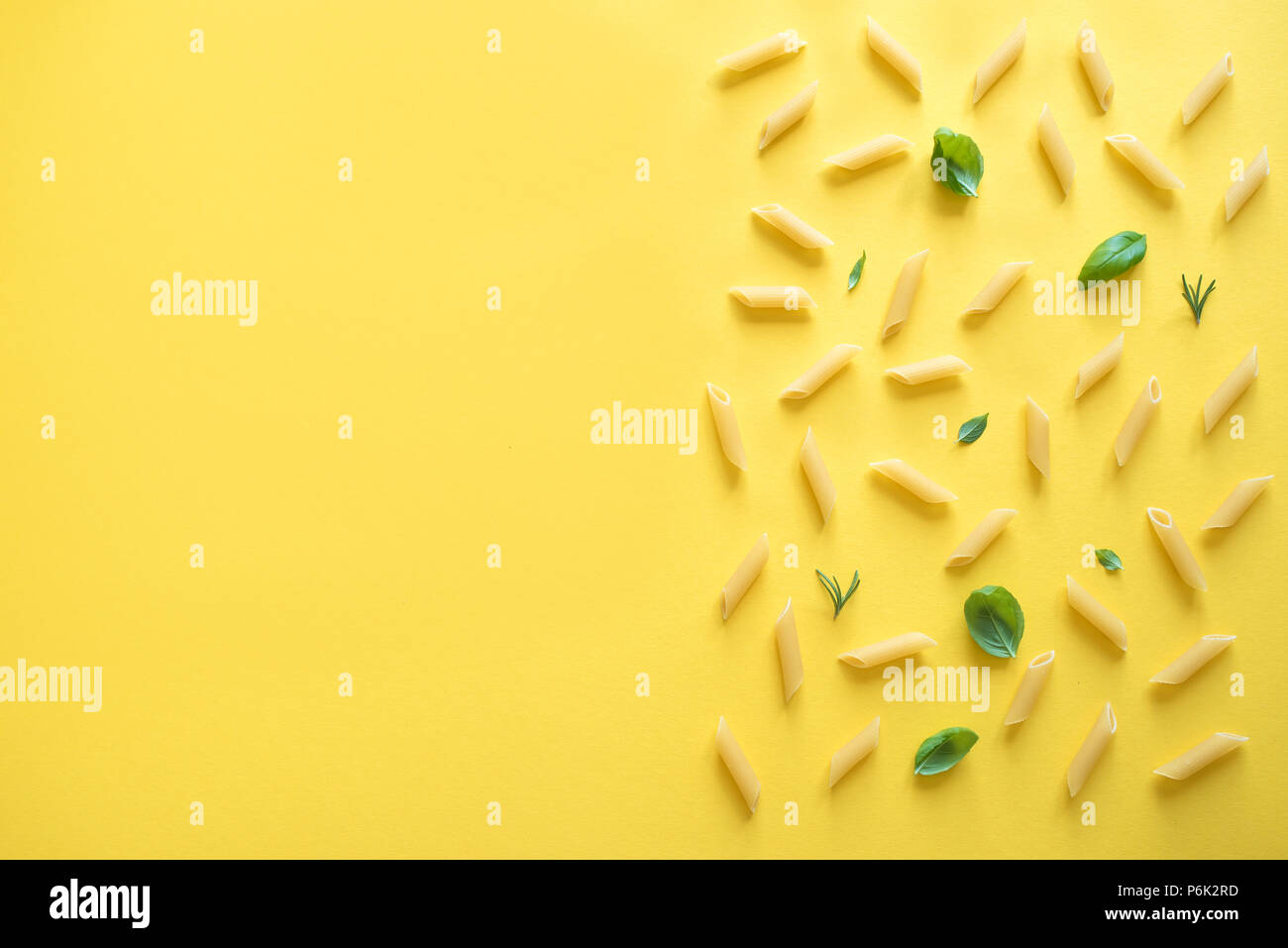 Penne Pasta su sfondo giallo, vista dall'alto, piatto laici. Pattern non cotti penne pasta con erbe aromatiche basilico e rosmarino. Foto Stock