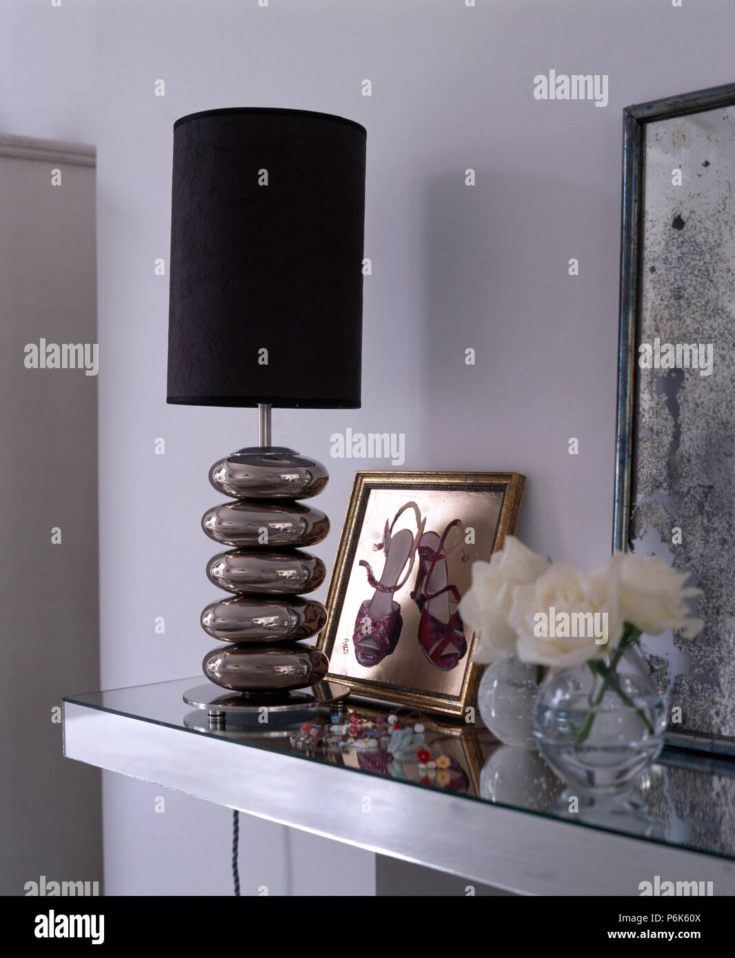 Tinta di nero su un vetro di lampada di ghiaia su un mantelpiece con un vaso di vetro di rose bianche Foto Stock