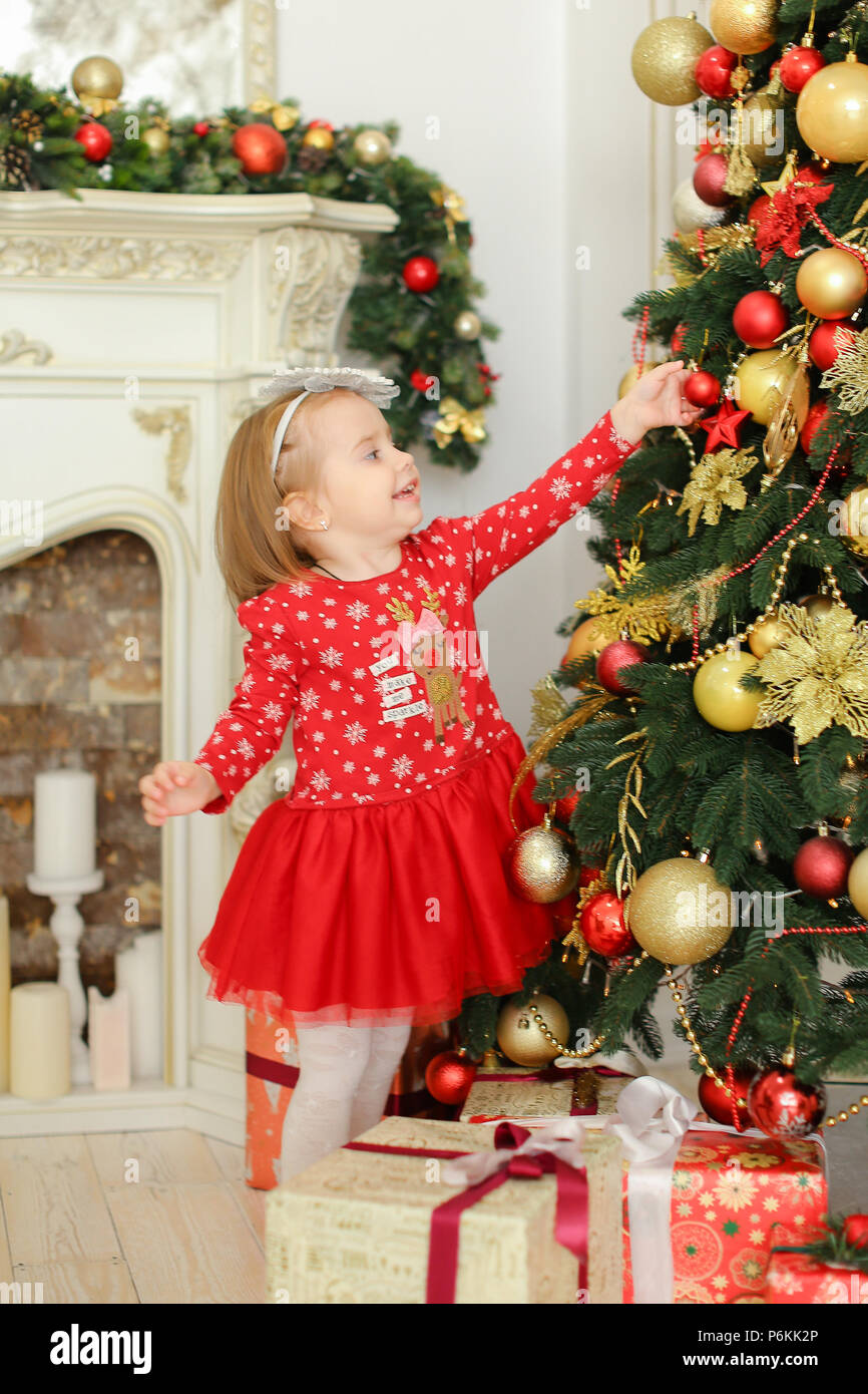 Bambina indossa abito rosso decorare albero di Natale vicino al camino e  presenta Foto stock - Alamy