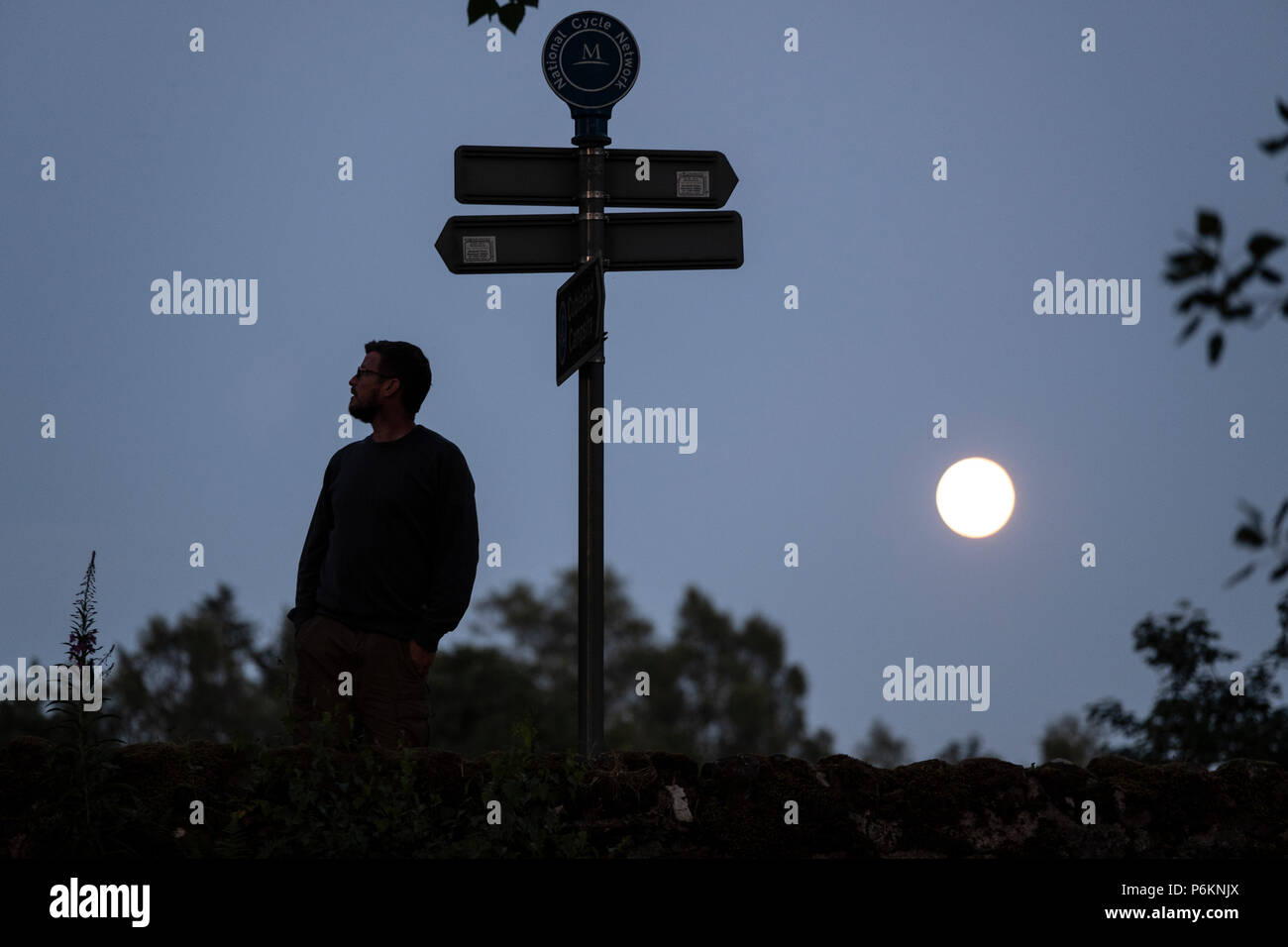 Un uomo mette in pausa per visualizzare un cartello stradale al chiaro di luna vicino Dunmuck nelle Highlands Scozzesi. Foto Stock