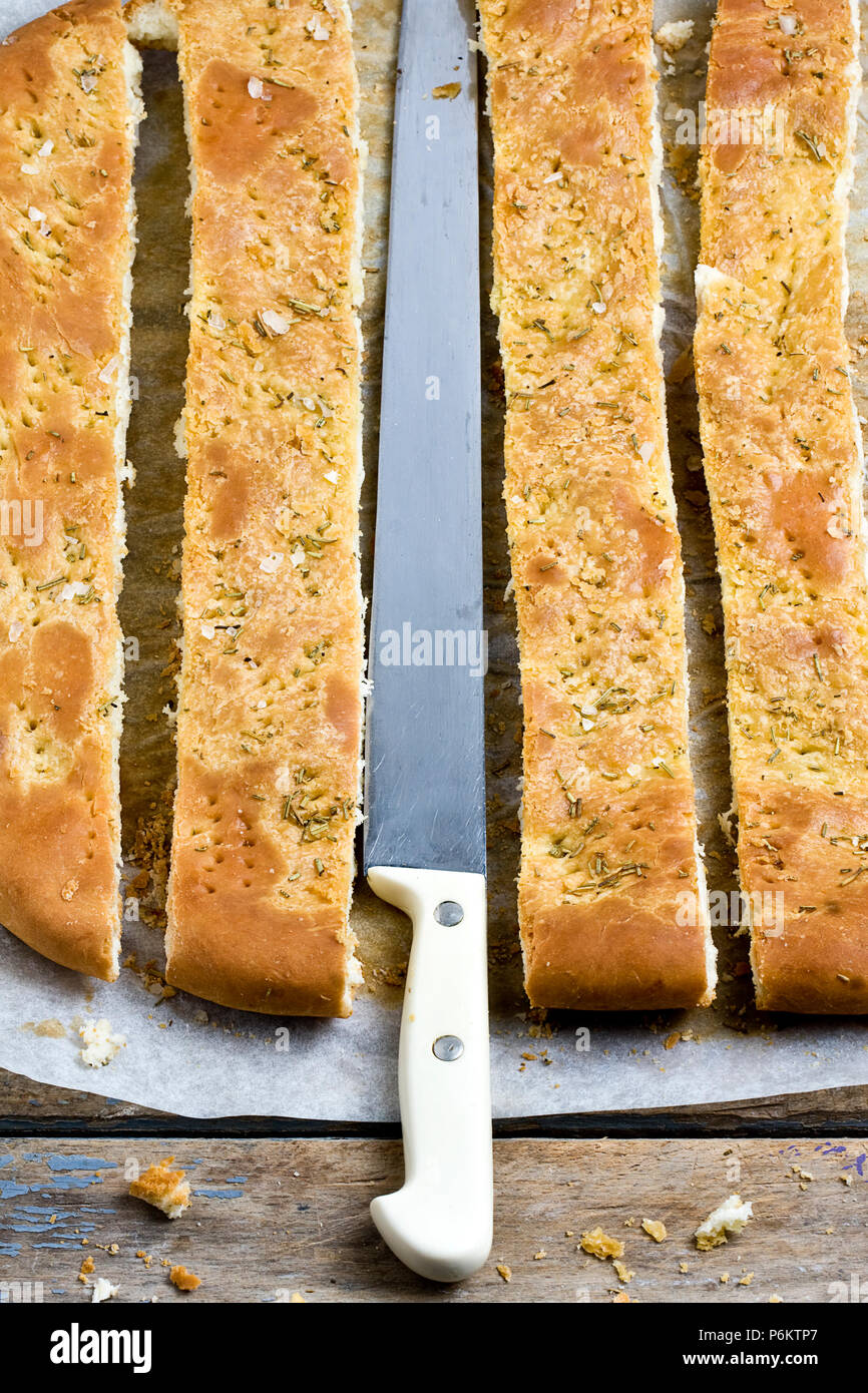 Vista dall'alto di fettine di pane foccacia con rosmarino e il coltello nel centro sul legno tavolo rustico Foto Stock