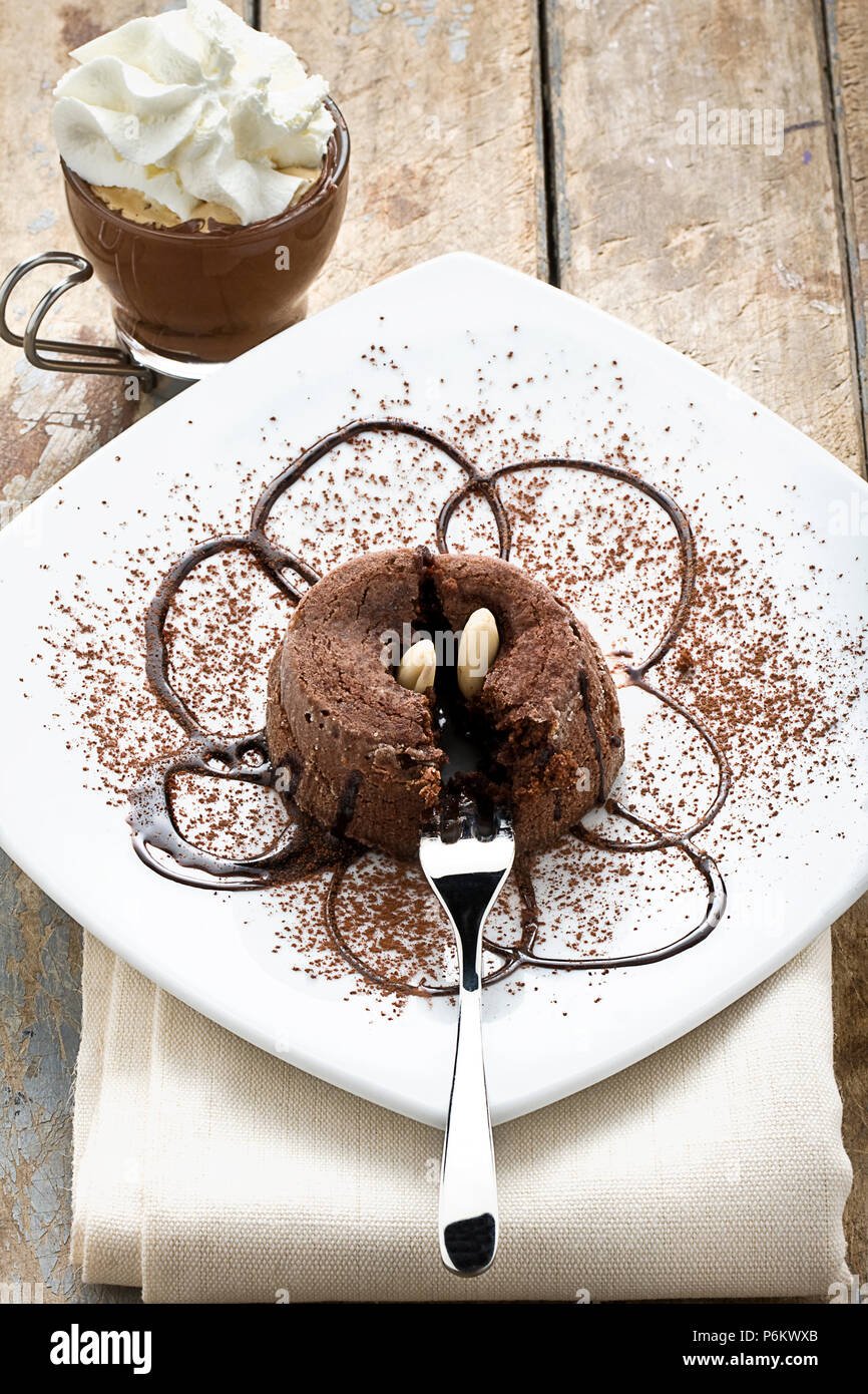 Dolce al cioccolato torta decorata con lo sciroppo al cioccolato mandorle e cacao in polvere e la tazza di caffè espresso con panna montata su legno tavolo rustico Foto Stock
