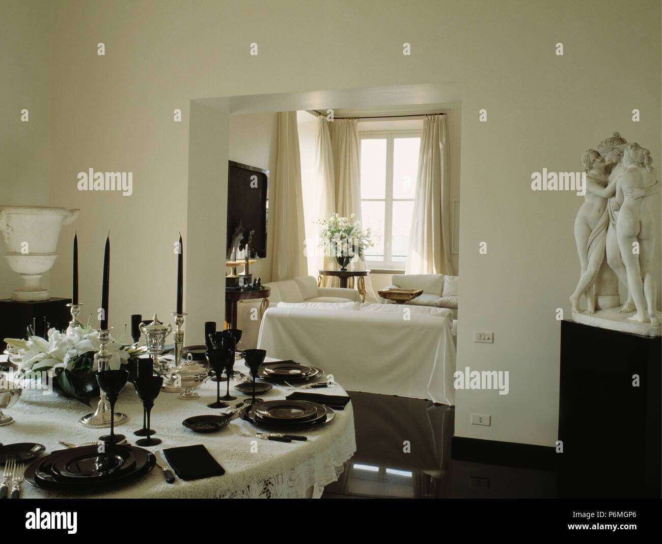 Le piastre nere e occhiali sulla tovaglia bianca in bianco sala da pranzo con statua classica in un angolo della stanza Foto Stock