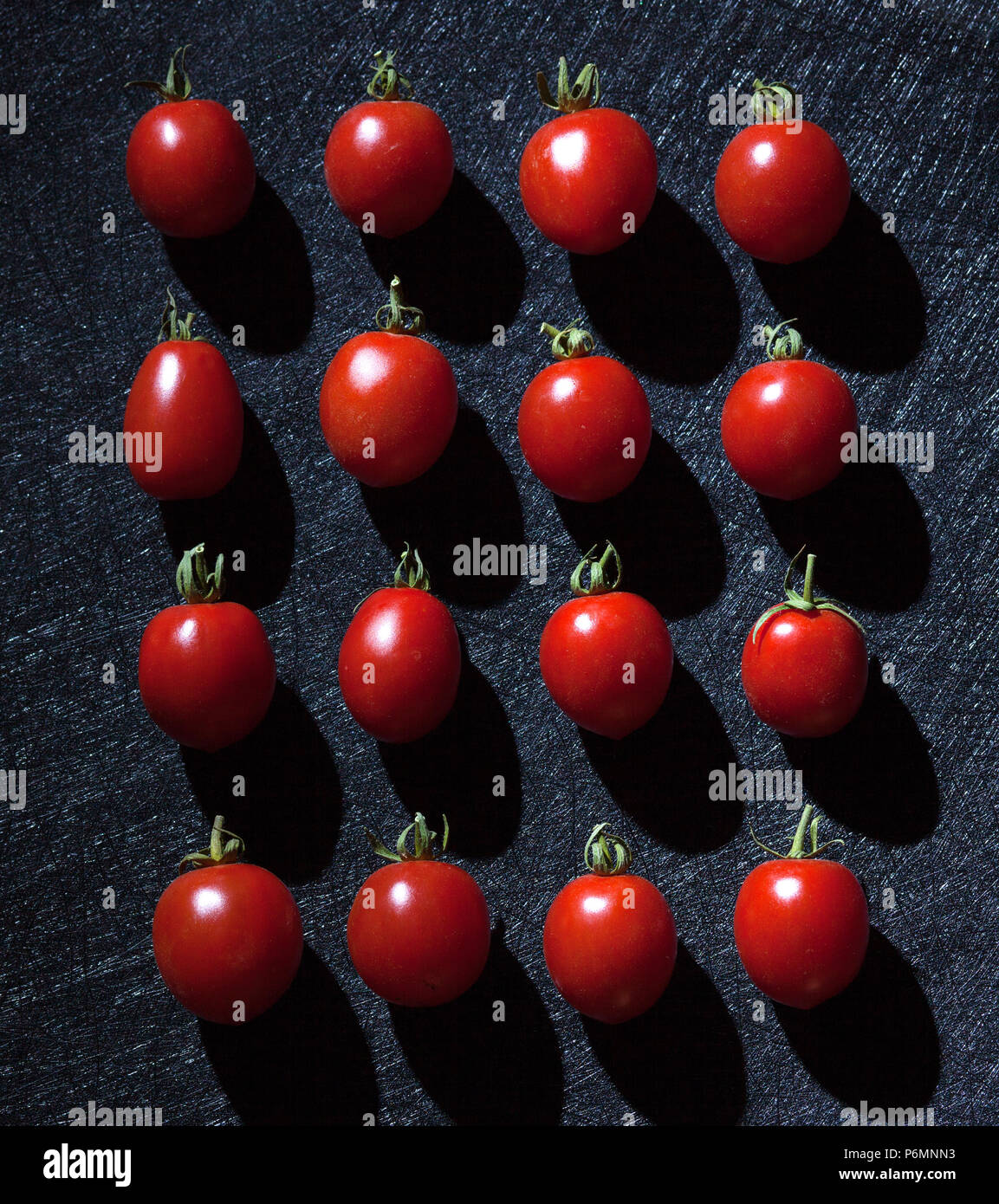 Crudo fresco di pomodori ciliegia su sfondo nero disposti in modo lineare. Foto Stock