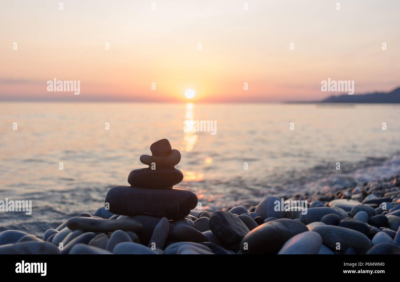 Piramide piegata Zen pietre ghiaia sul mare spiaggia al tramonto Foto Stock