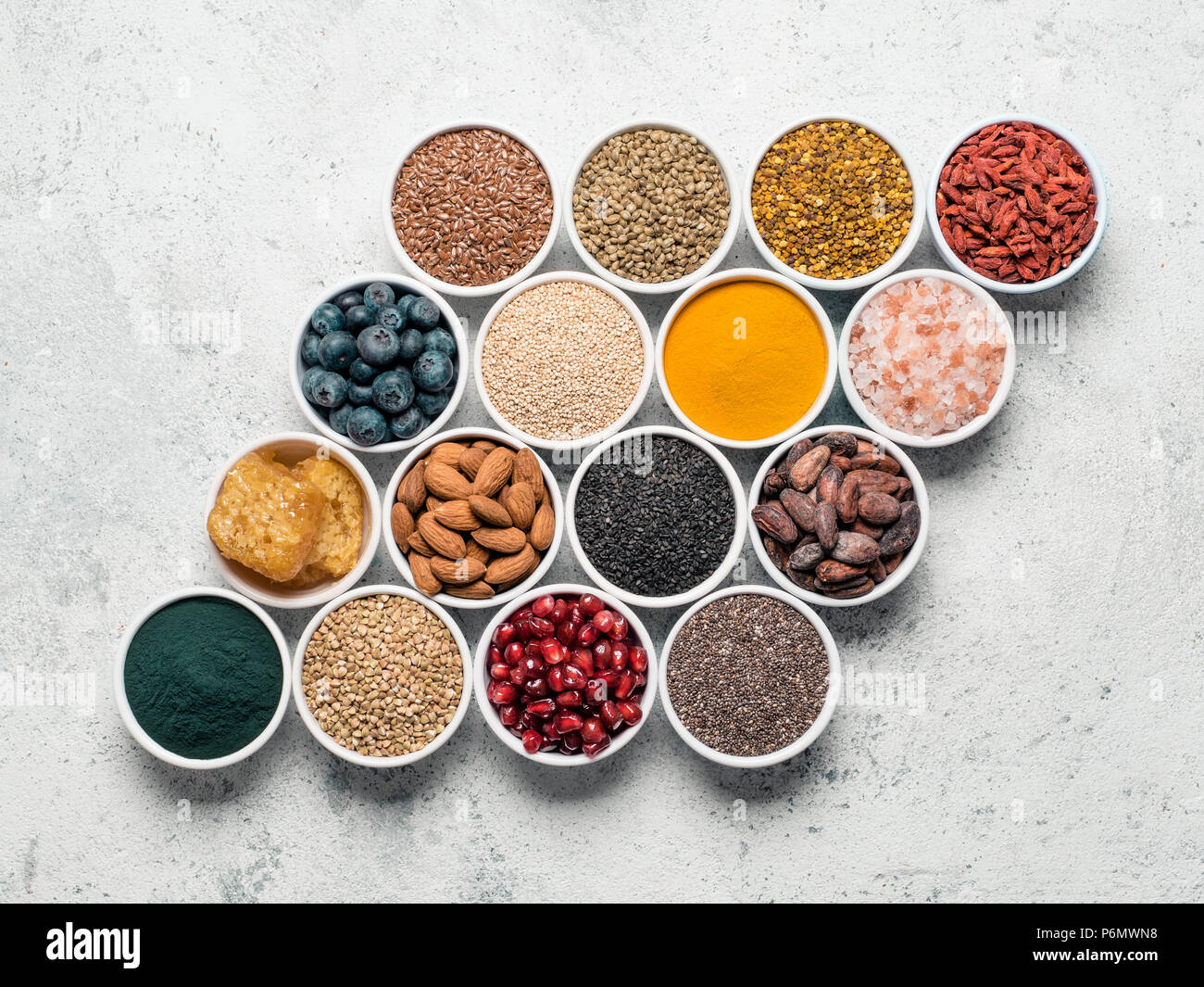 Varie superfoods nella piccola ciotola di cemento grigio Sfondo. Layout creativi di super come chia, spirulina, materie fava di cacao, goji, canapa, quinoa, bee pol Foto Stock