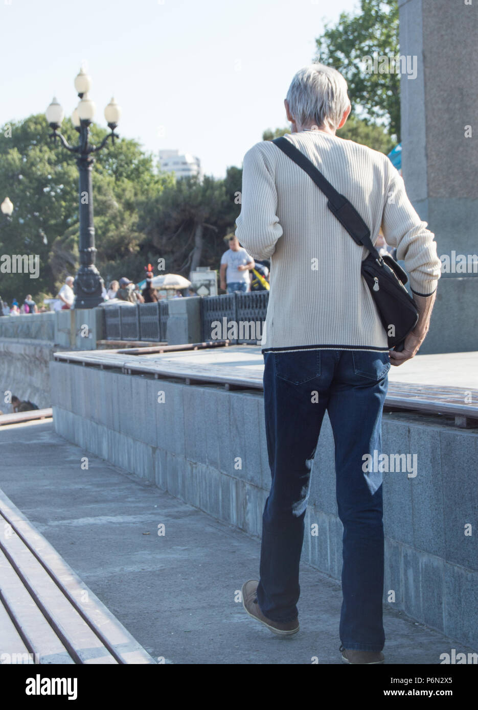 Grigio-dai capelli lunghi e sottili uomo anziano in jeans e maglione bianco  rapidamente cammina per la strada, la vista dal retro Foto stock - Alamy