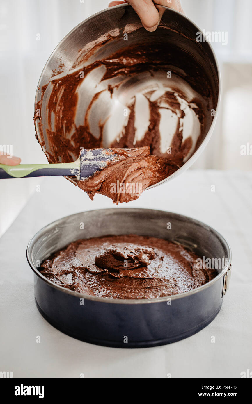 Torta al cioccolato impasto di essere trasferito in una forma tondeggiante  teglia con spatola in silicone. Donna preparare una torta al cioccolato per  essere cotto al forno. Backgroun bianco Foto stock -