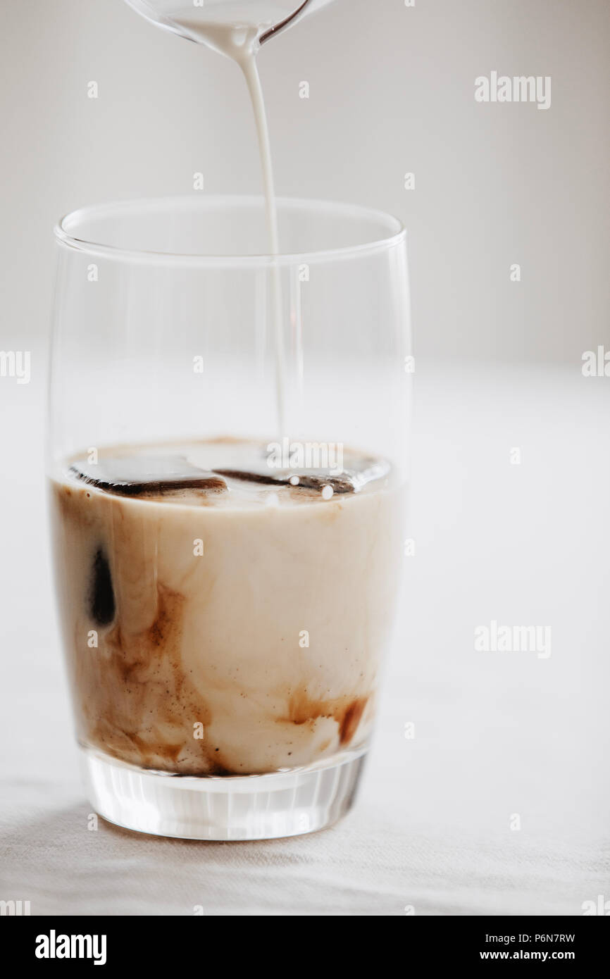 Caffè congelato di cubetti di ghiaccio in un bicchiere versato con latte  per fare un estivo rinfrescante caffè ghiacciato bere. Sfondo bianco,  vicino Foto stock - Alamy