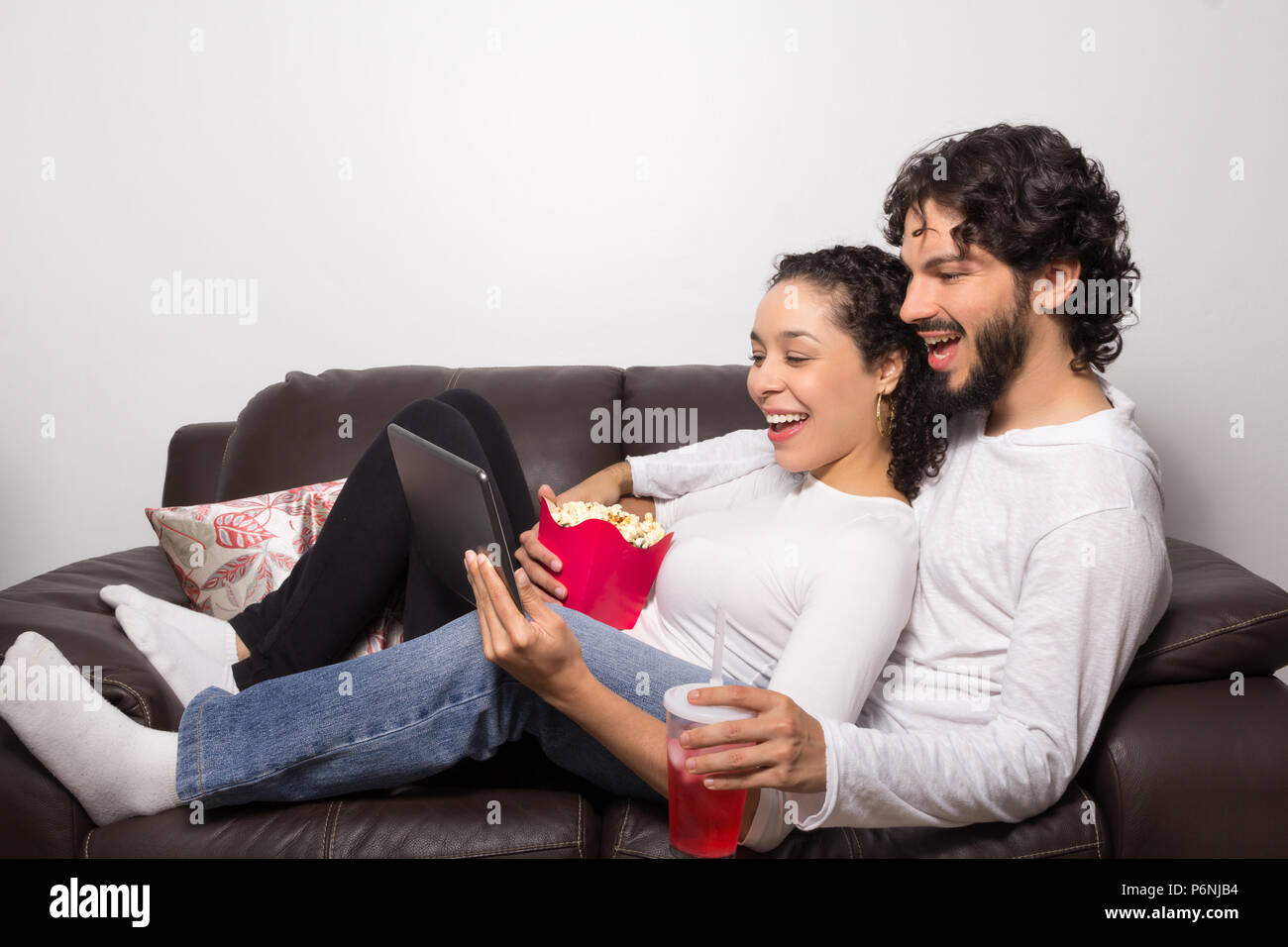Giovane sdraiato orologi sul video digitale compressa. L uomo e la donna  sono sempre sorridenti. Essi sono sul divano di casa di riposo. Le attività  per il tempo libero e stare insieme