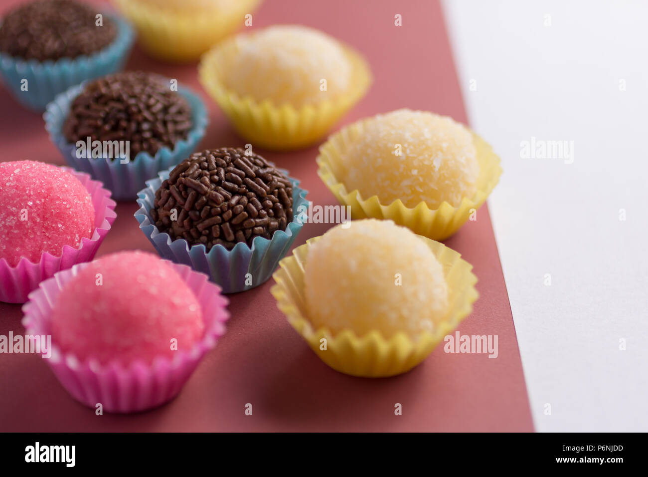 Caramelle brasiliano: Brigadeiro, Beijinho e Bicho de Pe. Bambini festa di compleanno. Le sfere di caramelle in una linea retta. Sfondo colorato. Foto Stock