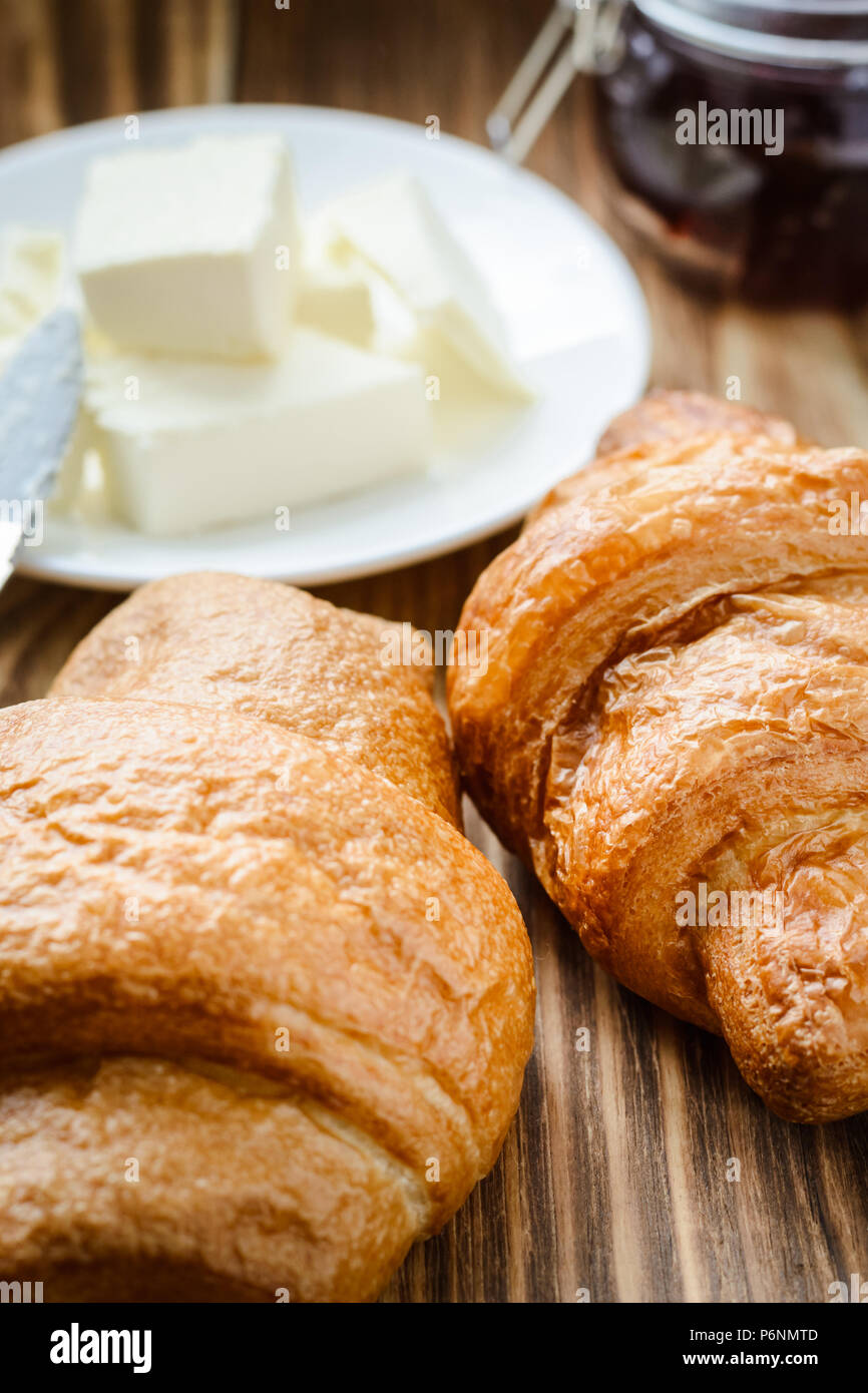 Due cornetti, burro e marmellata la mattina un tavolo di legno. Prima colazione francese Foto Stock