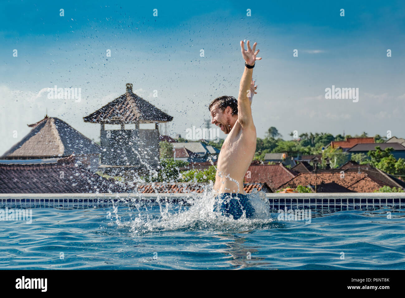 Estate vita - molto felice, snello giovane uomo sorridente, saltando fuori acqua di piscina con schizzi, sul tetto ed in alto le mani. Emozioni - la gioia, la felicità. Foto Stock