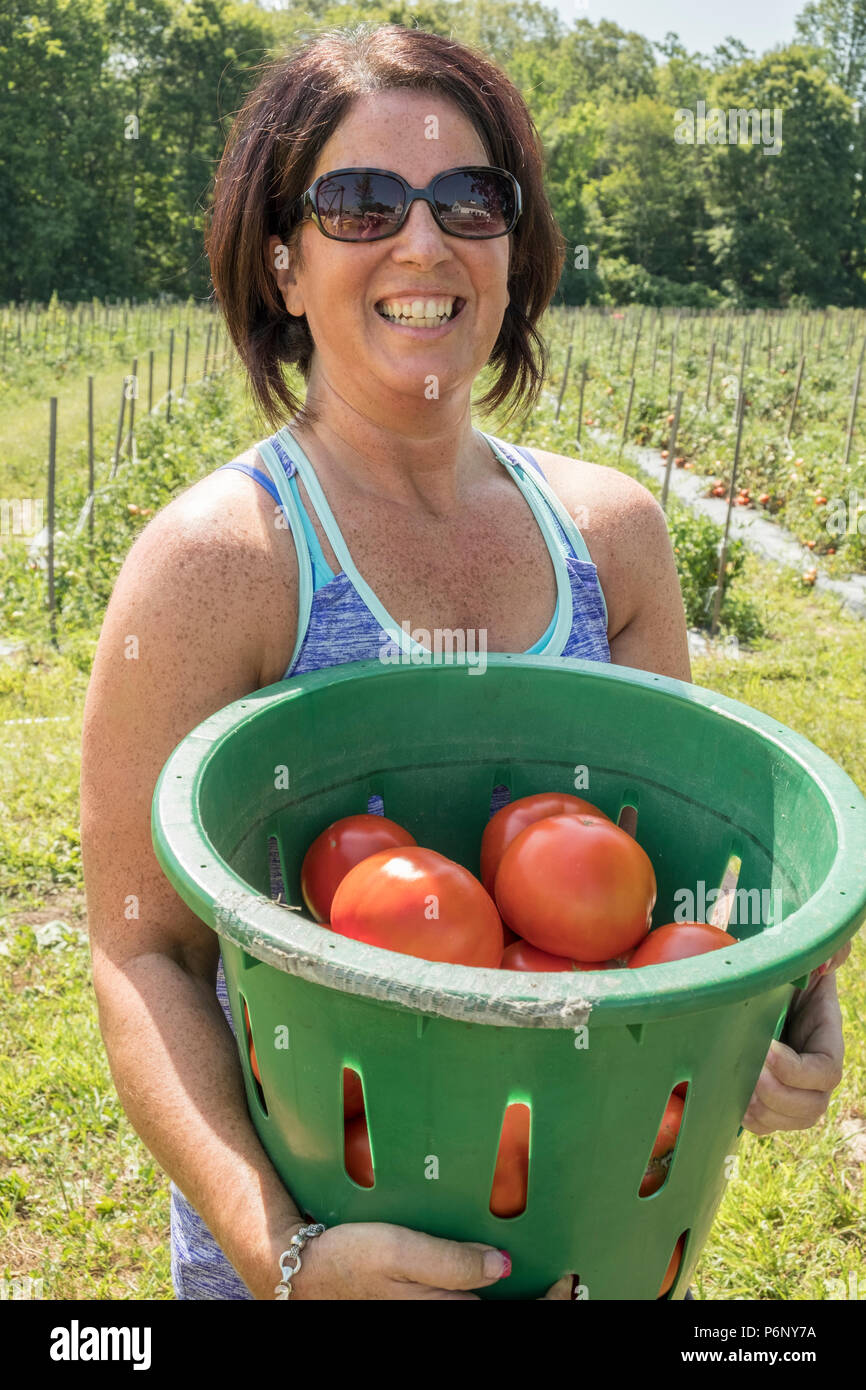 Una donna felice con un cesto di pomodori che ha appena preso.portante Foto Stock