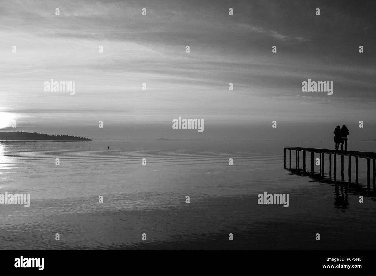 Un giovane su un molo sul lago al tramonto, con il sole che scende dietro e isola Foto Stock