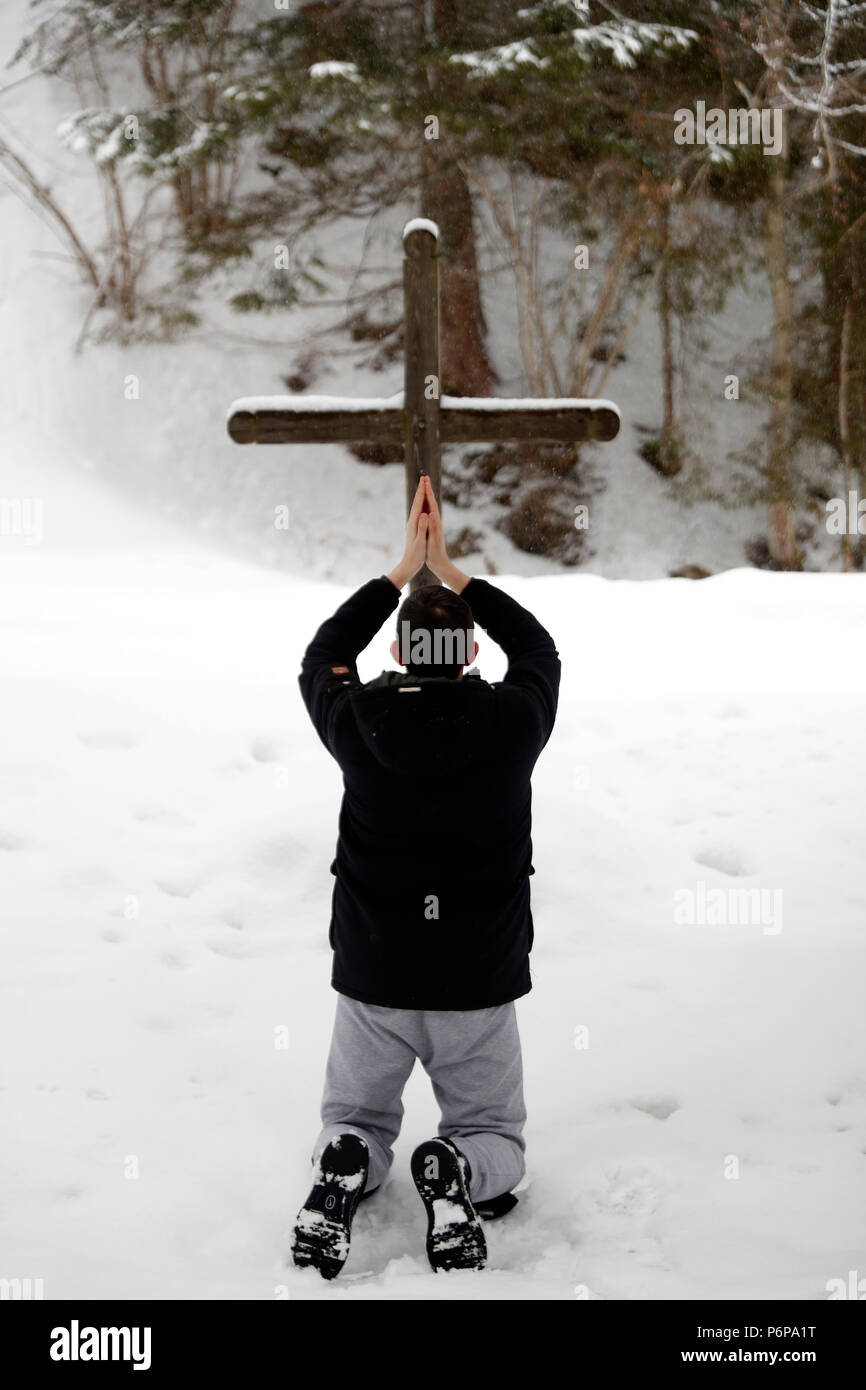 Ragazzo cristiano pregare in inverno davanti a una croce di legno. Les Contamines. La Francia. Foto Stock