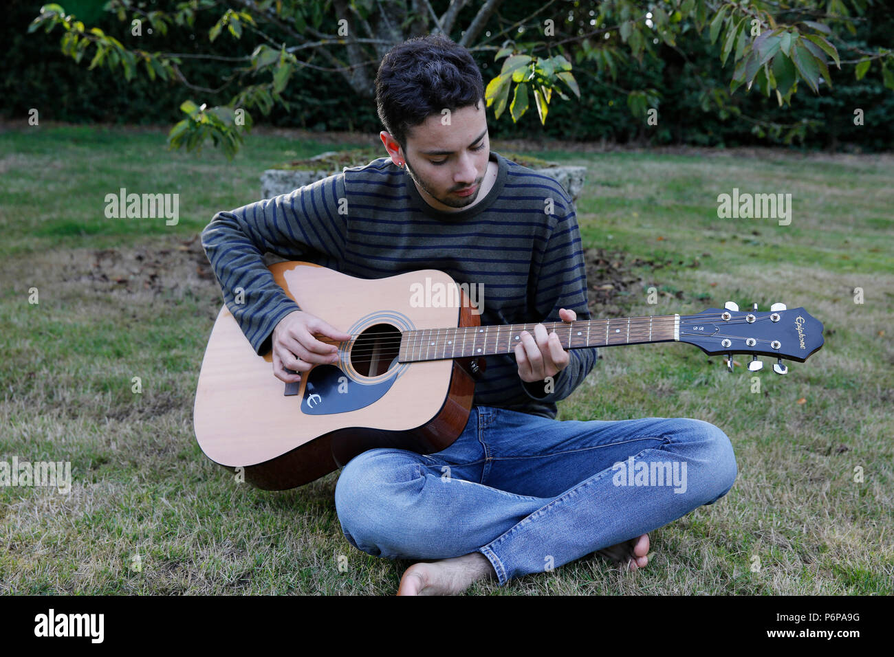 Giovane uomo di suonare una chitarra in un giardino. La Francia. Foto Stock