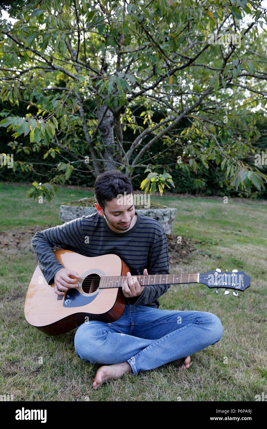 Giovane uomo di suonare una chitarra in un giardino. La Francia. Foto Stock