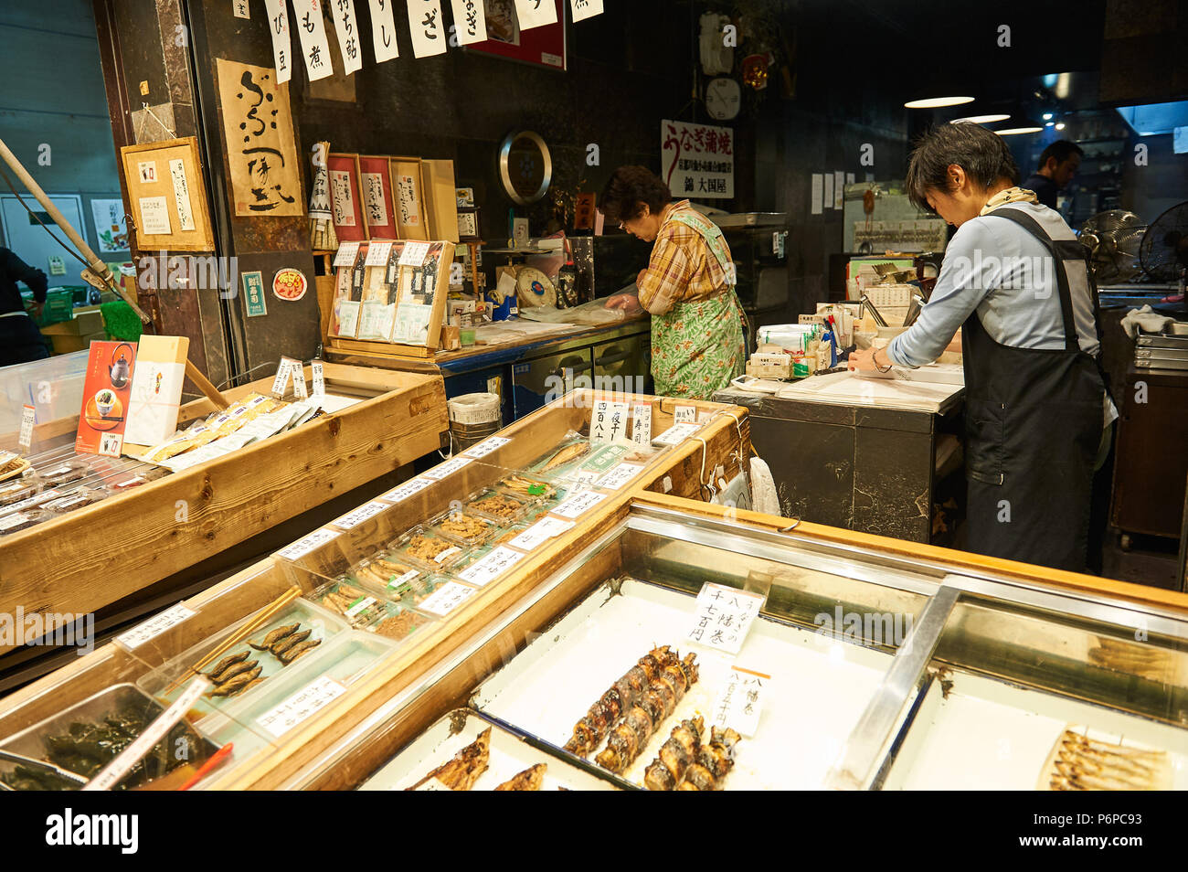 Mercato Nishiki, Kyoto: un pescivendolo negozio vendita varietà di pesce cucinato in molti modi. Un cliente sguardi intorno come il suo ordine è stato avvolto ordinatamente. Foto Stock