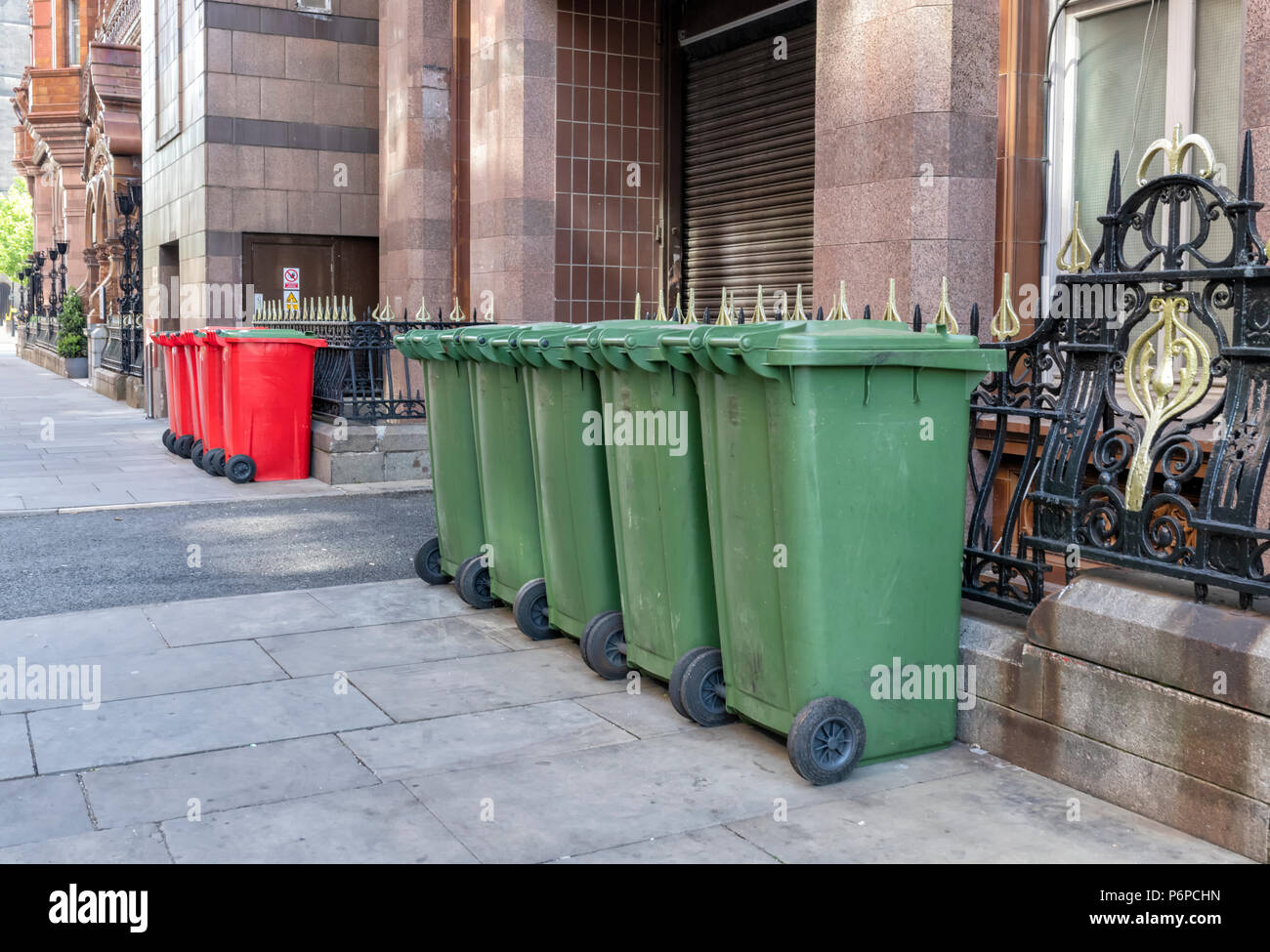 Una fila di 6 rosso e 5 verde scomparti wheelie sul marciapiede in una strada nel centro della città di Manchester, Regno Unito Foto Stock