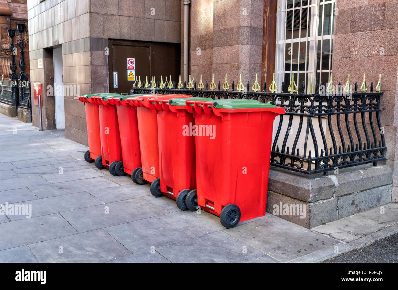 Una fila di 6 rosso e 5 verde scomparti wheelie sul marciapiede in una strada nel centro della città di Manchester, Regno Unito Foto Stock