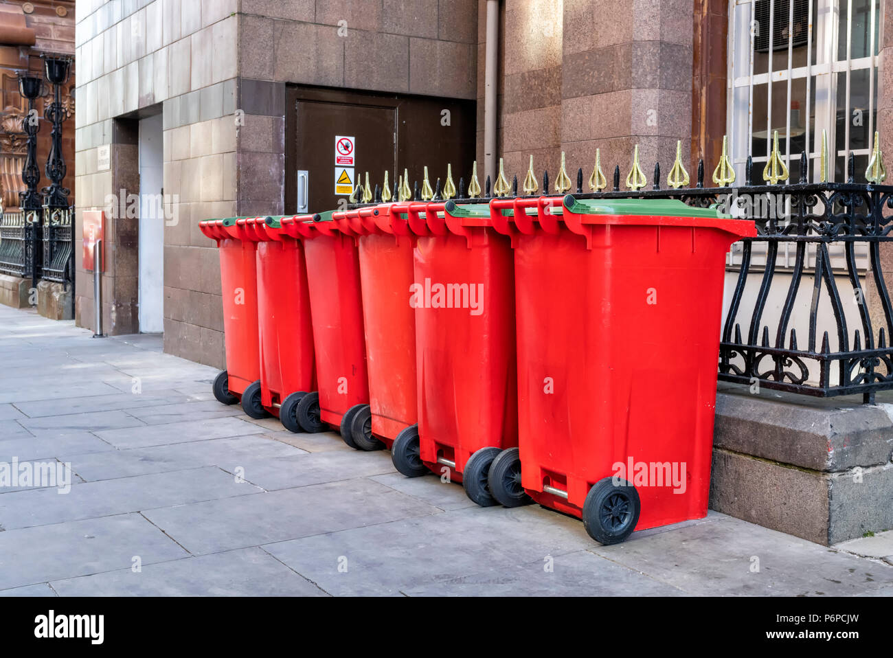 Una fila di 6 rosso scomparti wheelie sul marciapiede in una strada nel centro della città di Manchester, Regno Unito Foto Stock
