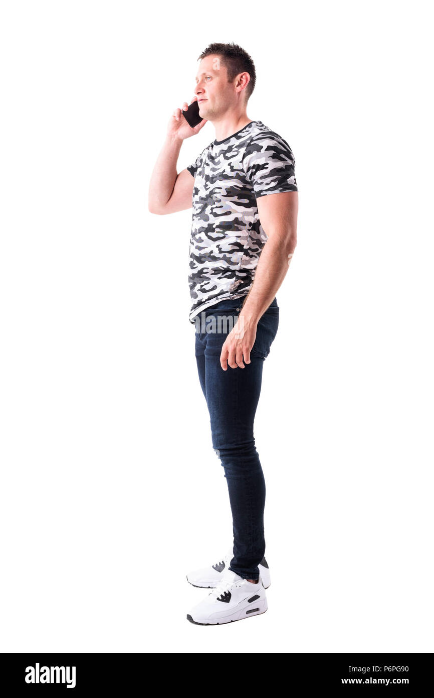 Vista laterale del fiducioso uomo adulto in camo t-shirt parlando al telefono cellulare e guardando lontano. Corpo pieno isolati su sfondo bianco. Foto Stock