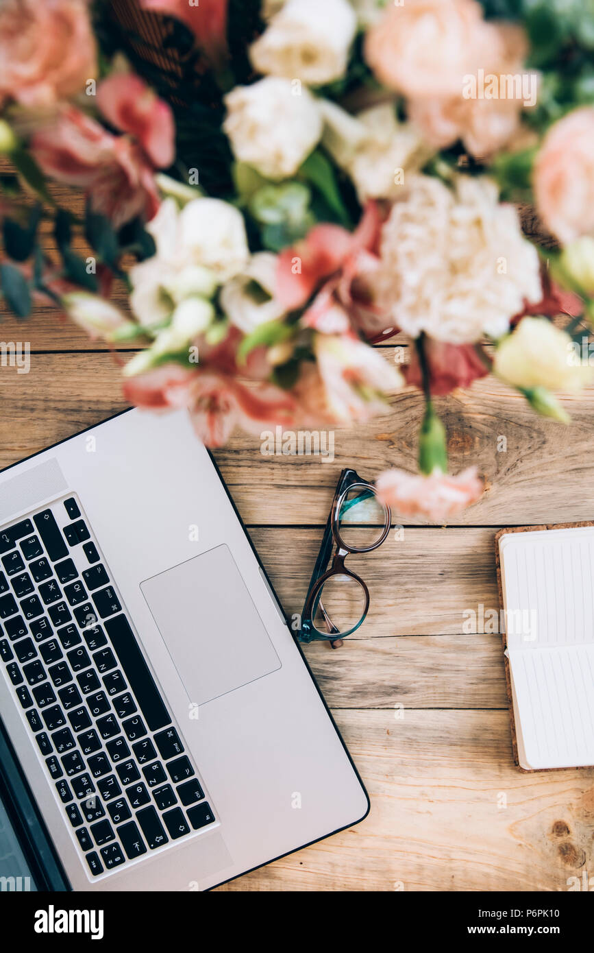 Office Workplace essentials: laptop, notebook carta, bicchieri e un mazzo di fiori sulla tavola in legno rustico sfondo Foto Stock Office Workplace essentials: laptop, notebook carta, bicchieri e un mazzo di fiori sulla tavola in legno rustico sfondo Foto Stock