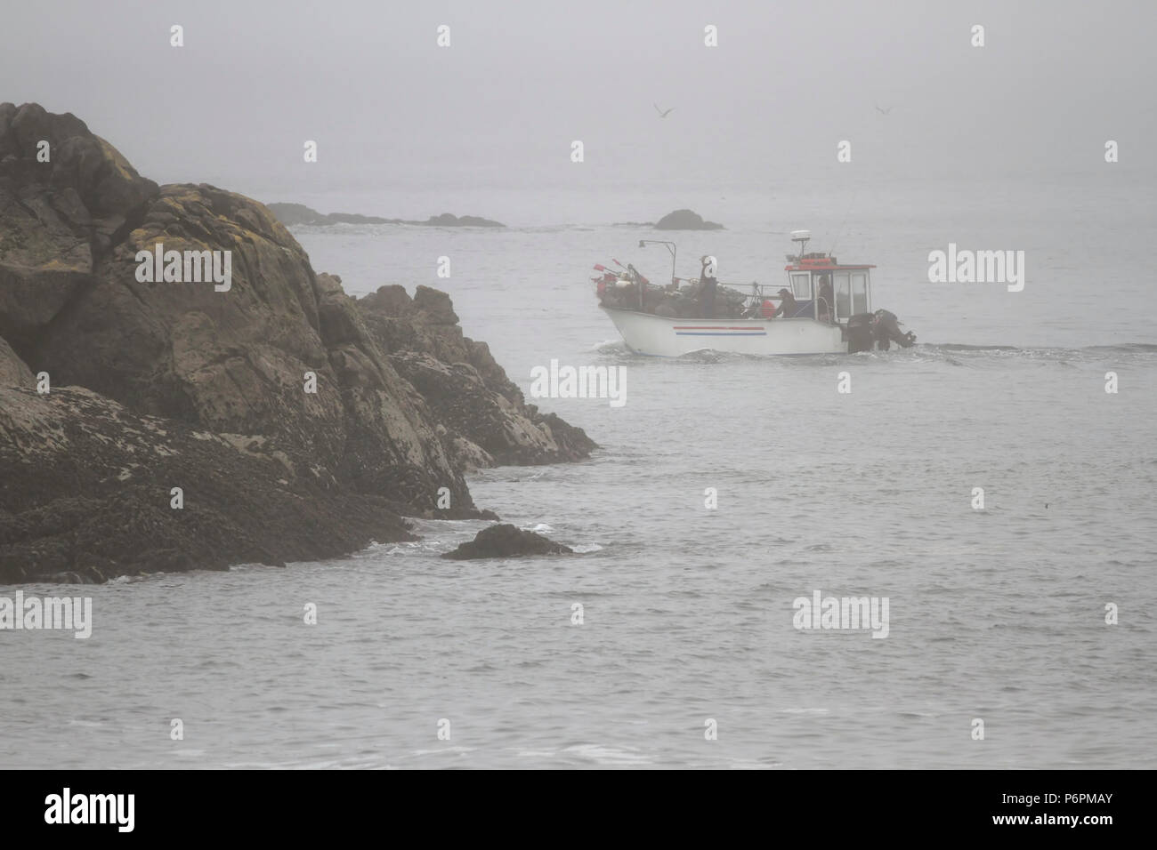 Portoghese tradizionale piccola barca da pesca nella fatica tra massi. Portoghese settentrionale costa rocciosa in un estate mattinata nebbiosa. Foto Stock