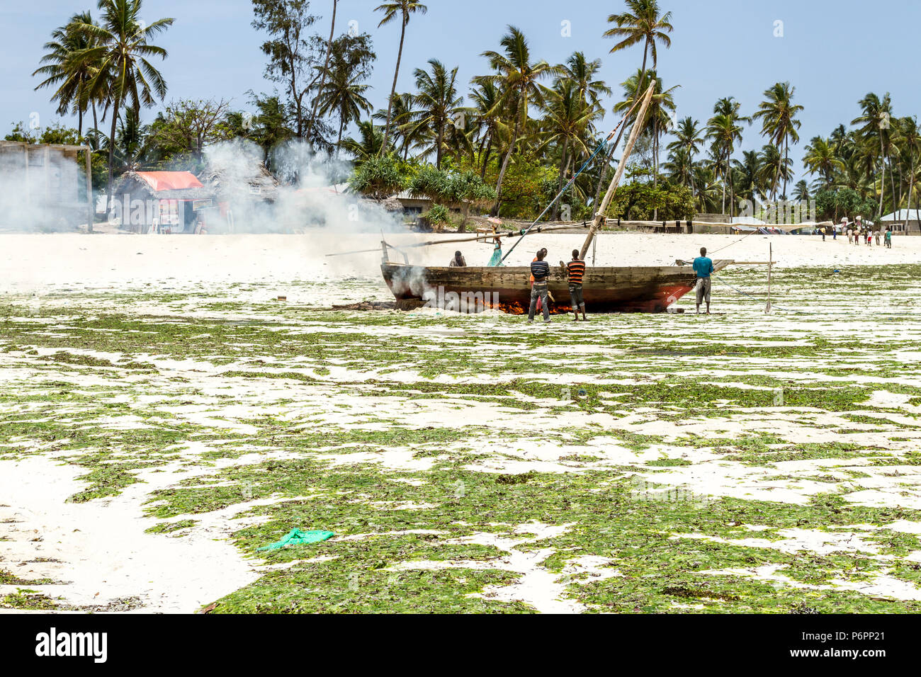 I pescatori di Zanzibar eseguendo riparazioni dal fuoco di un dhow tradizionale vela , barca da pesca. Foto Stock