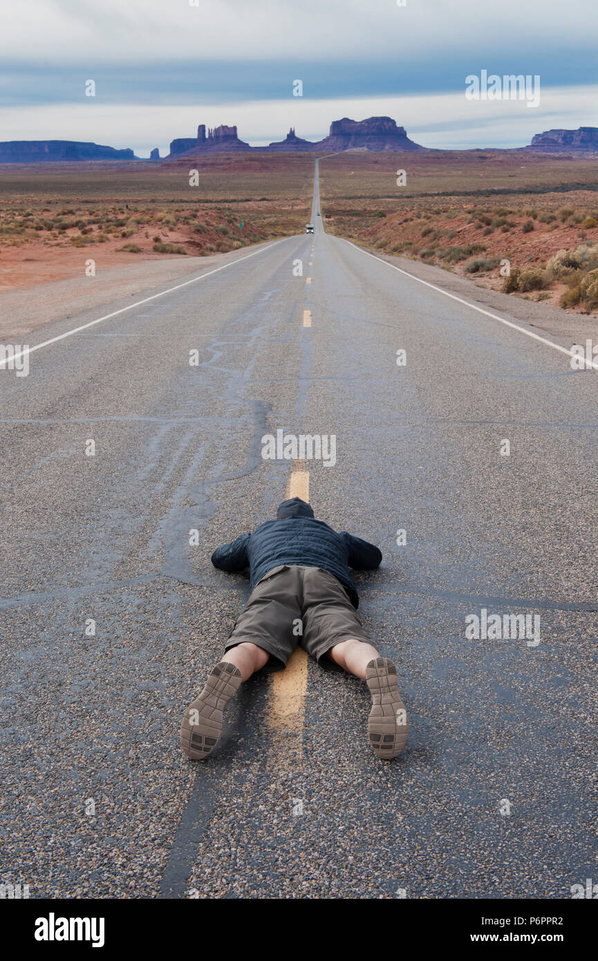 L'uomo che giace piatto su il suo ventre per scattare una foto della strada statale 163 che conduce alla Monument Valley, Arizona, Stati Uniti. Foto Stock