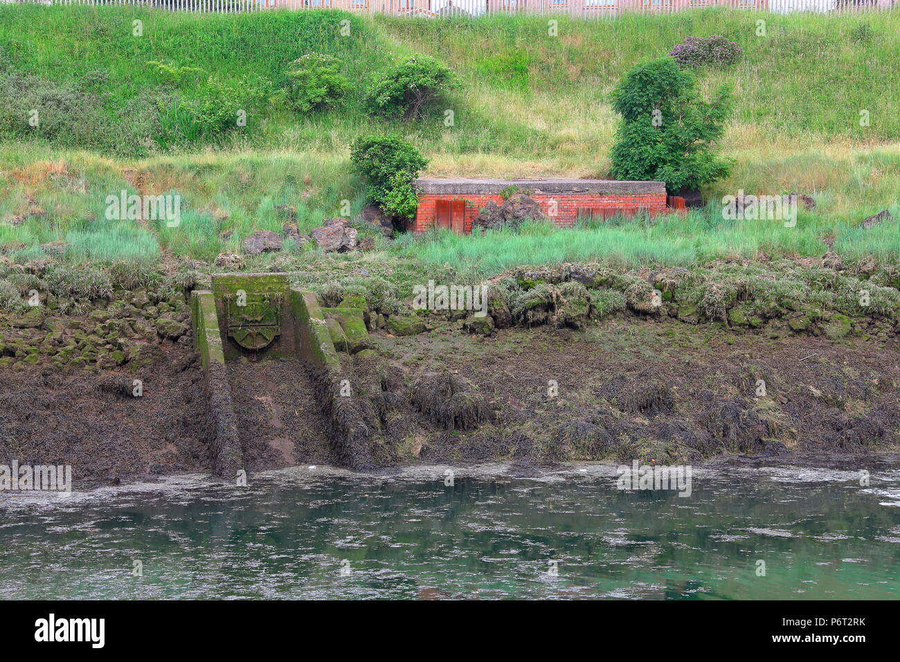 Una ghisa acqua valvola di controllo con calcestruzzo di uno scalo per più di acqua che scorre per viaggiare verso il basso nel fiume di marea di seguito. Foto Stock