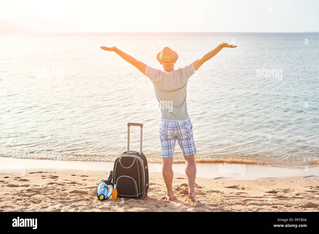 L'uomo turistico in abiti estivi con una valigia in mano, guardando il mare sulla spiaggia, il concetto di tempo per viaggiare Foto Stock
