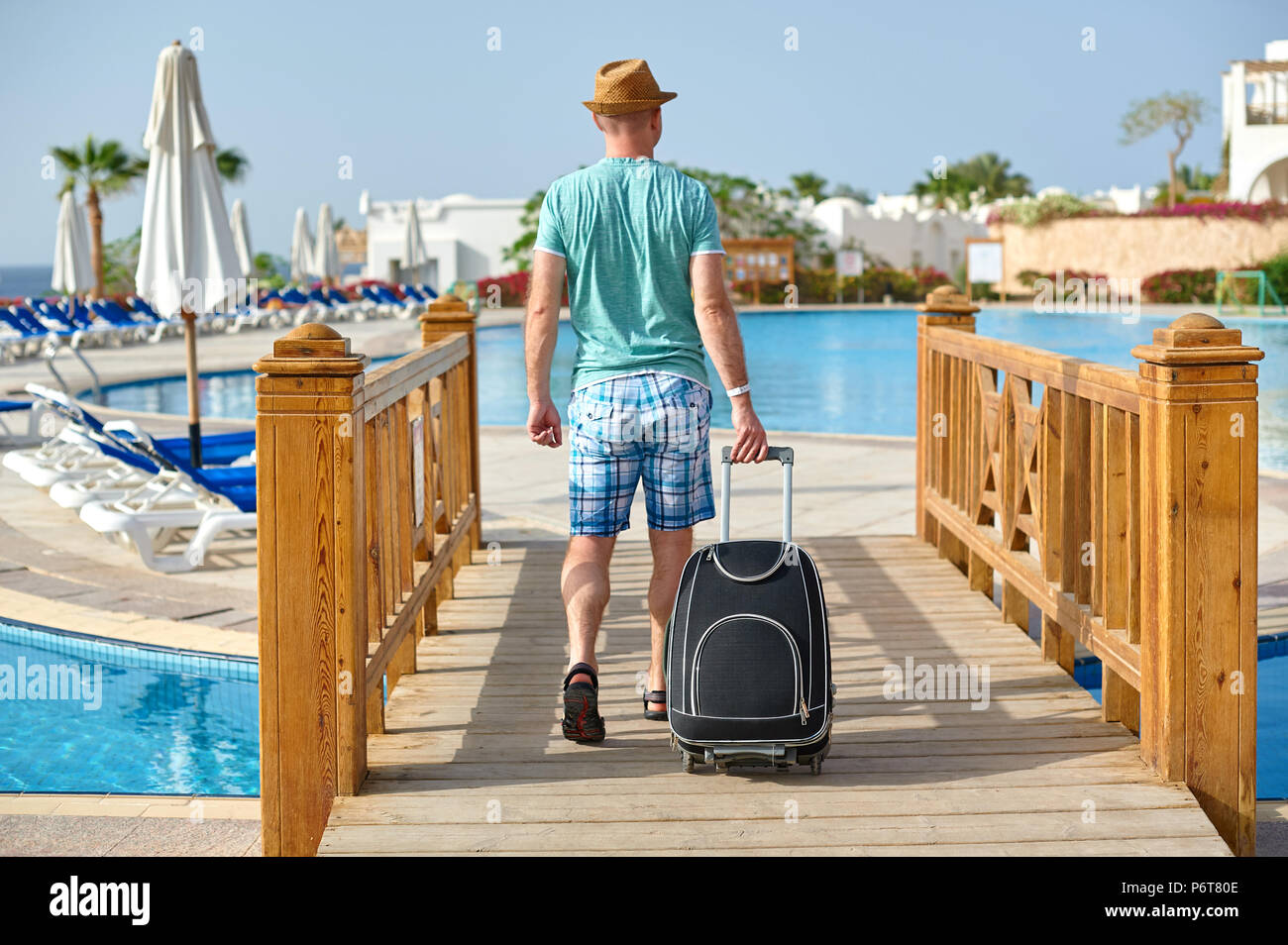 L'uomo turistico in abiti estivi con una valigia in mano, guardando il mare sulla spiaggia con piscina in hotel, il concetto di tempo per viaggiare Foto Stock