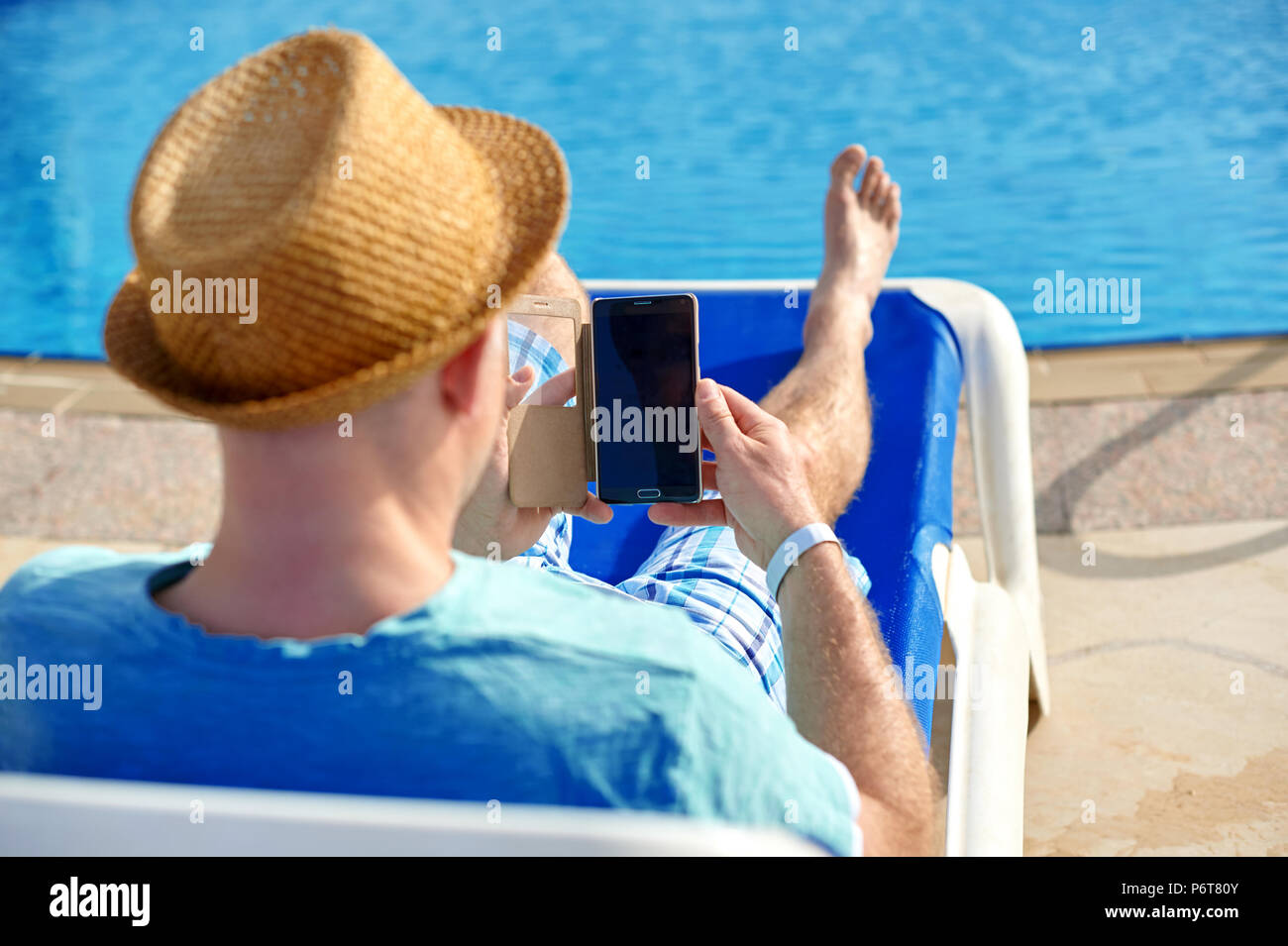 Uomo che utilizza il telefono cellulare in vacanza presso la piscina in hotel, il concetto di un libero professionista che lavora per se stesso su viaggi e vacanze Foto Stock