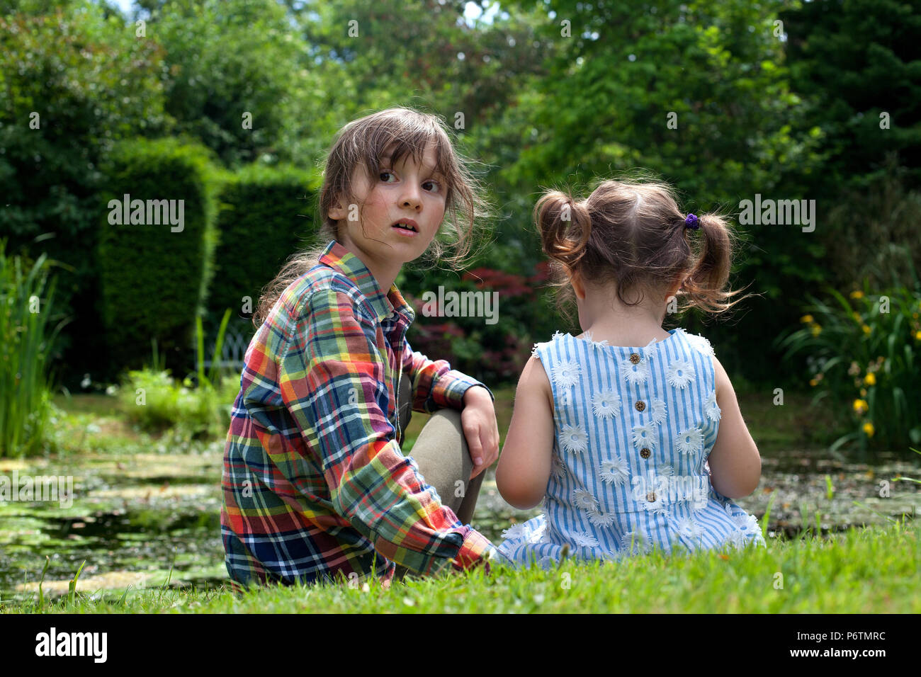Un ragazzo e una ragazza seduta da stagno guardando il bambino le rane. Foto Stock