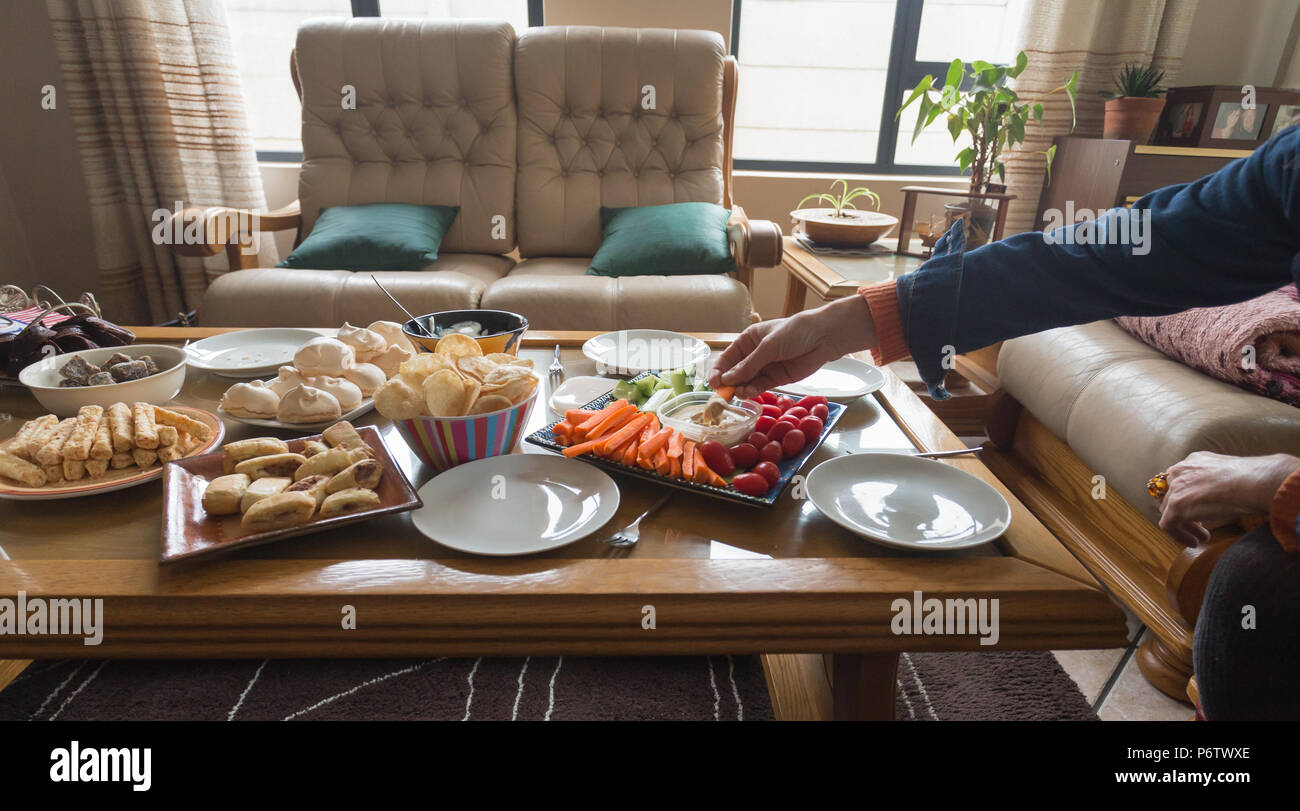 donna braccio e mano raggiungere per il cibo su un concetto di tavolo autentica e informale casa celebrazione e stile di vita Foto Stock
