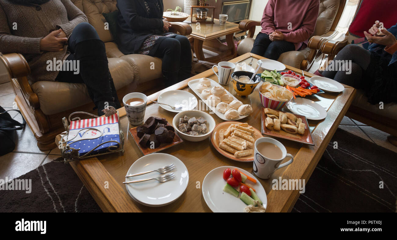 le donne che siedono intorno ad un tavolo di caffè riempito con una varietà di cibi o spuntini differenti che celebrano un compleanno informale nel paese Foto Stock