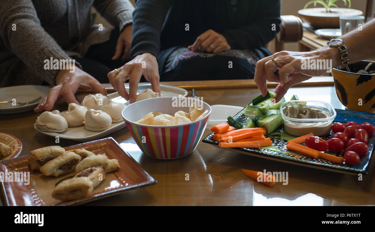 gruppo di mani delle donne che si raggiungono per raccogliere spuntini o cibo da un tavolo in una festa informale Foto Stock