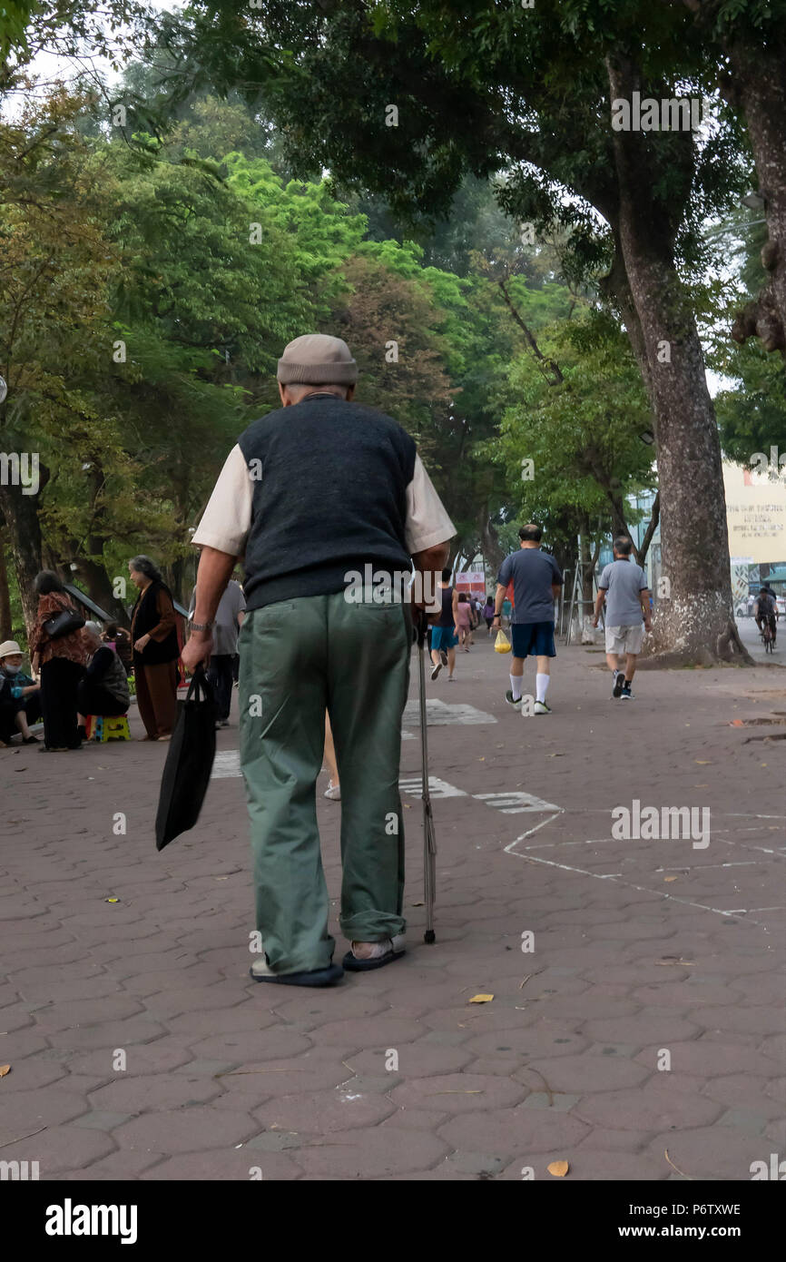 Uomo anziano a piedi, con l'aiuto di un bastone da passeggio, intorno al leggendario lago Hoan Kiem, Hanoi, Vietnam Foto Stock