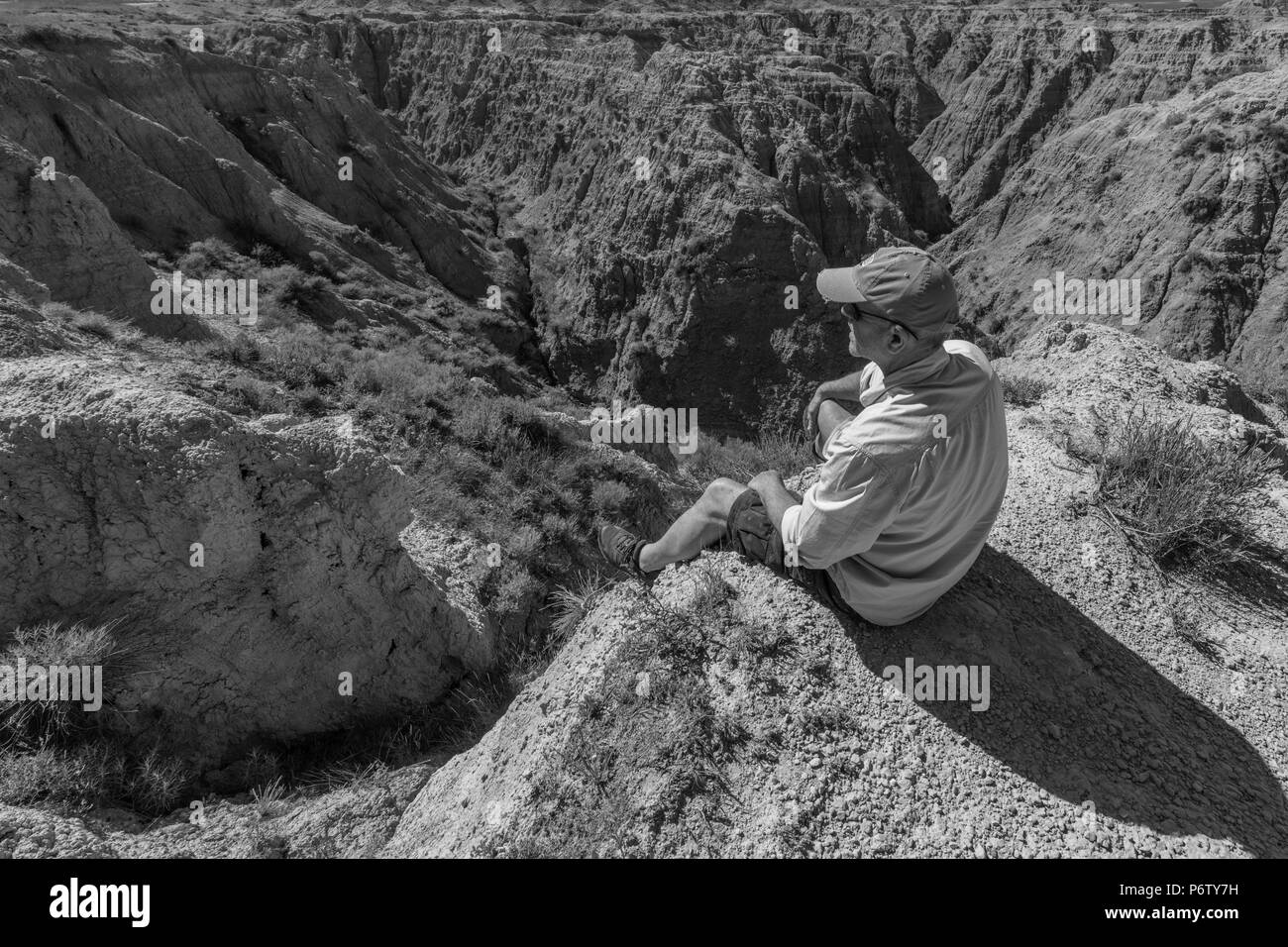Uomo seduto sul bordo del rock Parco nazionale Badlands, Dakota del Sud, STATI UNITI D'AMERICA Foto Stock