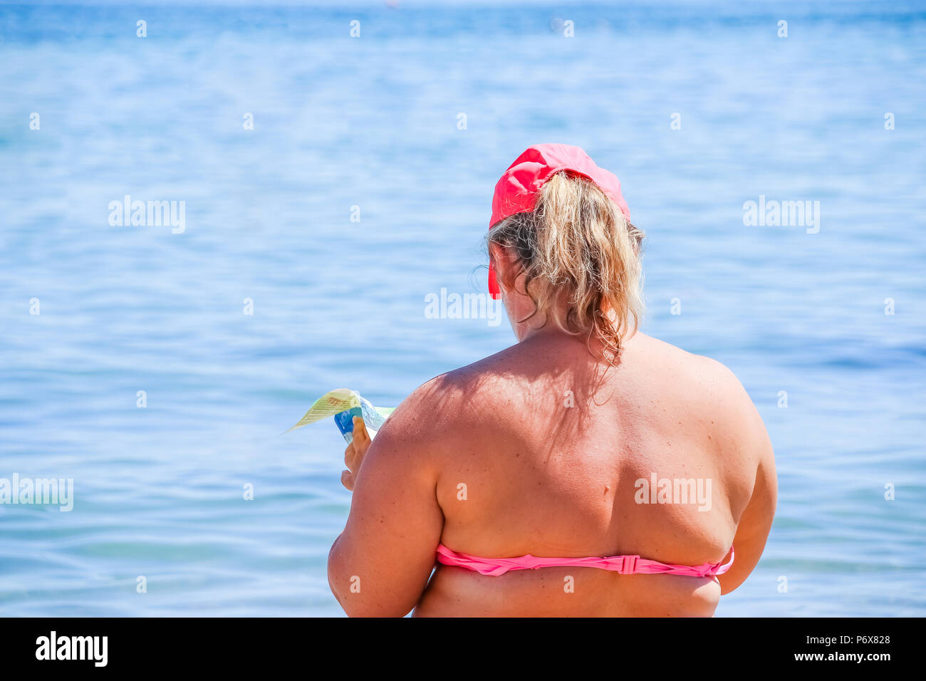 Donna matura in costume da bagno al mare. Il sovrappeso donna in costume da  bagno arriva sulla spiaggia, la lettura di un libro, vista posteriore.donne  grasse seduto su una spiaggia da un