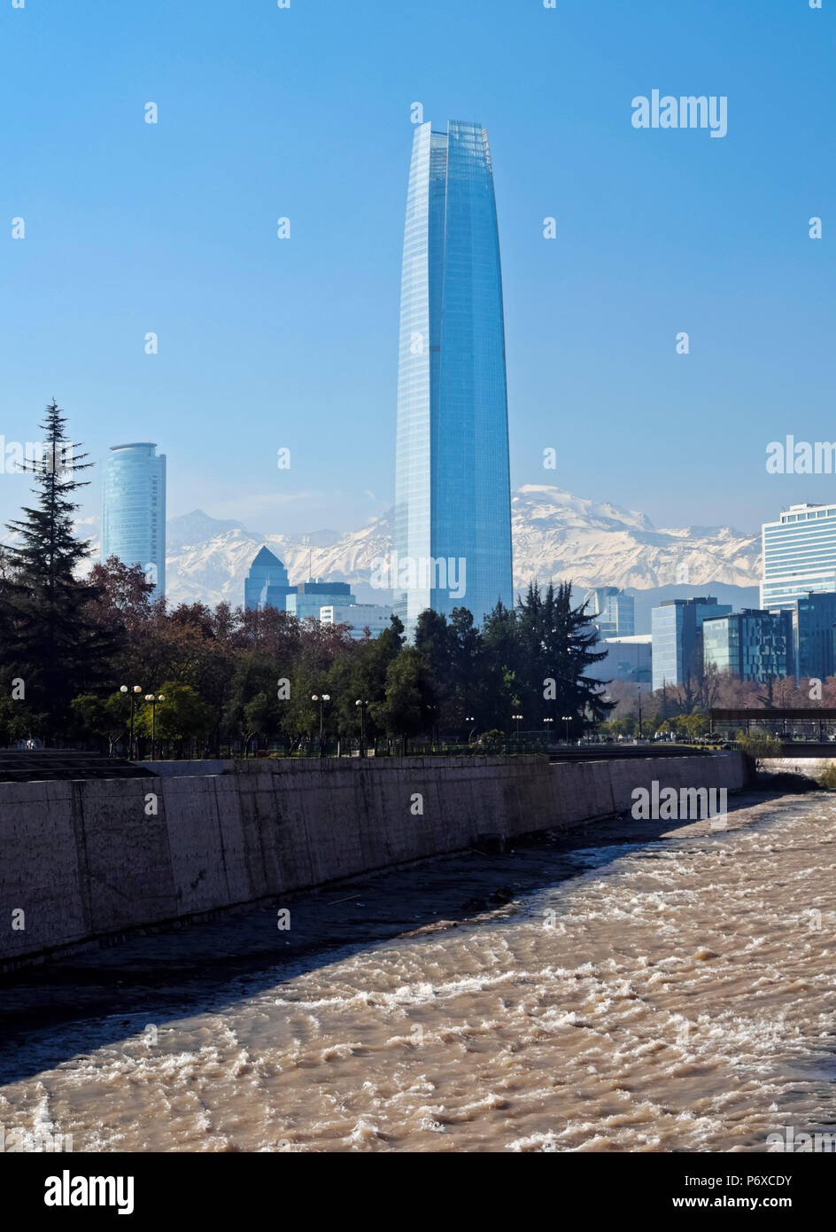 Il Cile, Santiago, vista sul fiume Mapocho, verso l'alto sollevato edifici con Costanera Center Tower, l'edificio più alto in Sud America. Coperta di neve Ande in background. Foto Stock